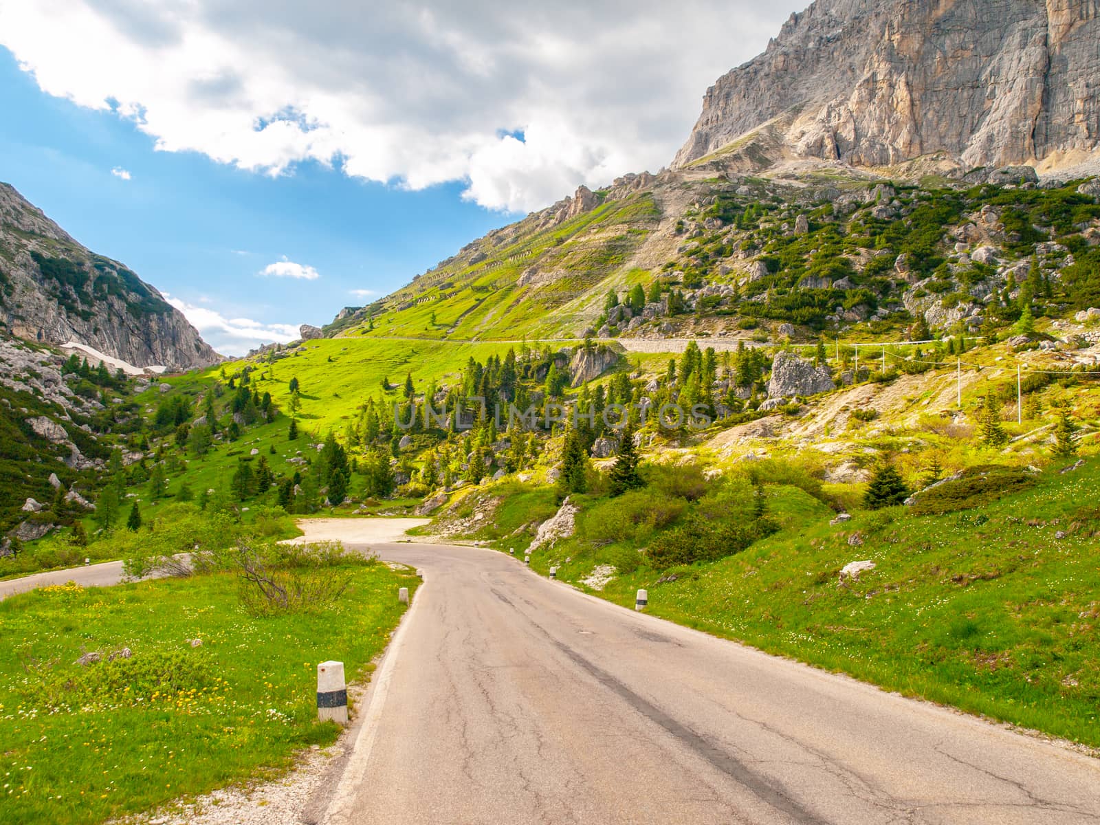 Asphalt road, green meadows and dolomite rocks at Passo Falzarego, Dolomites, Italy.