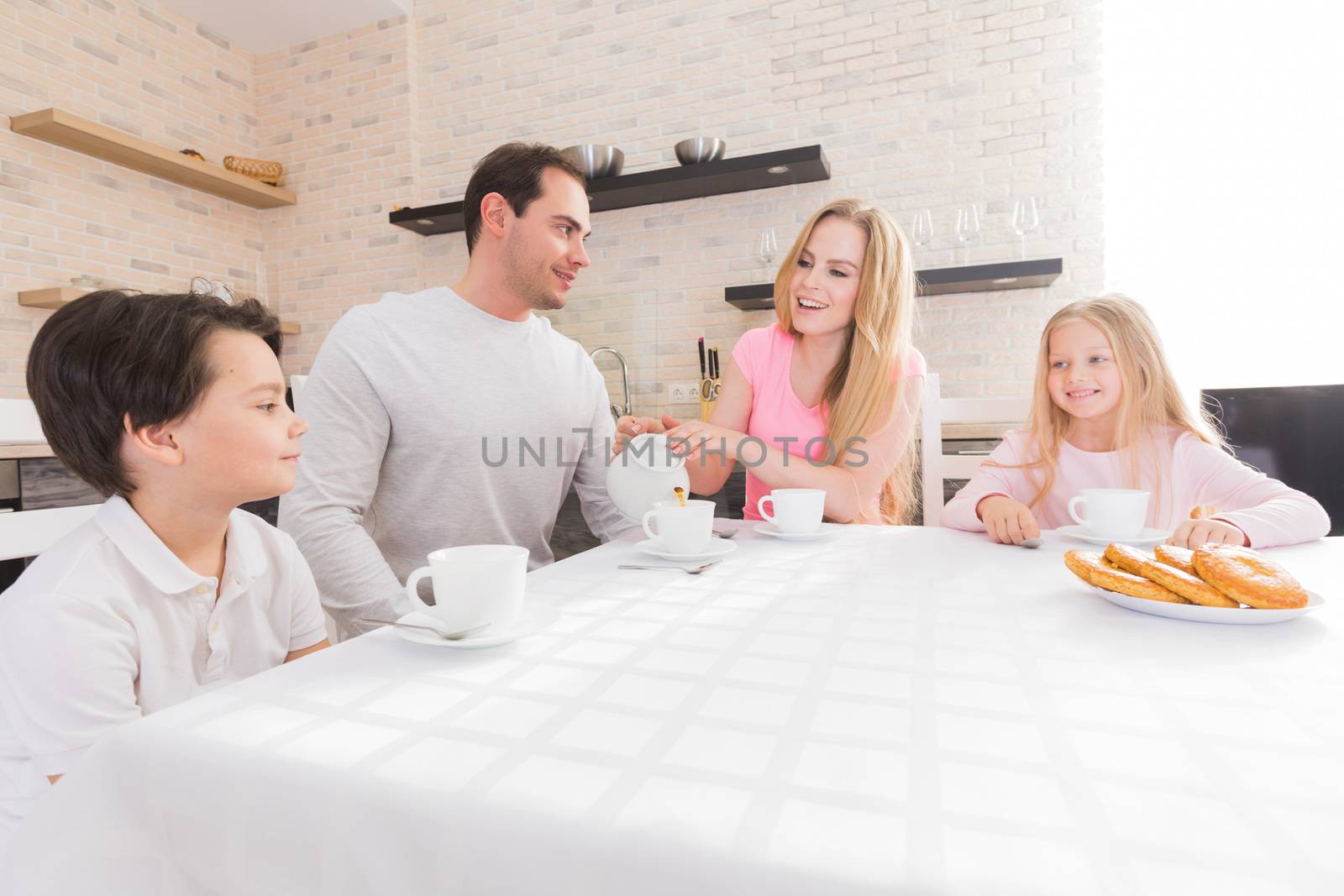 Family eating cookies with tea in the kitchen at home