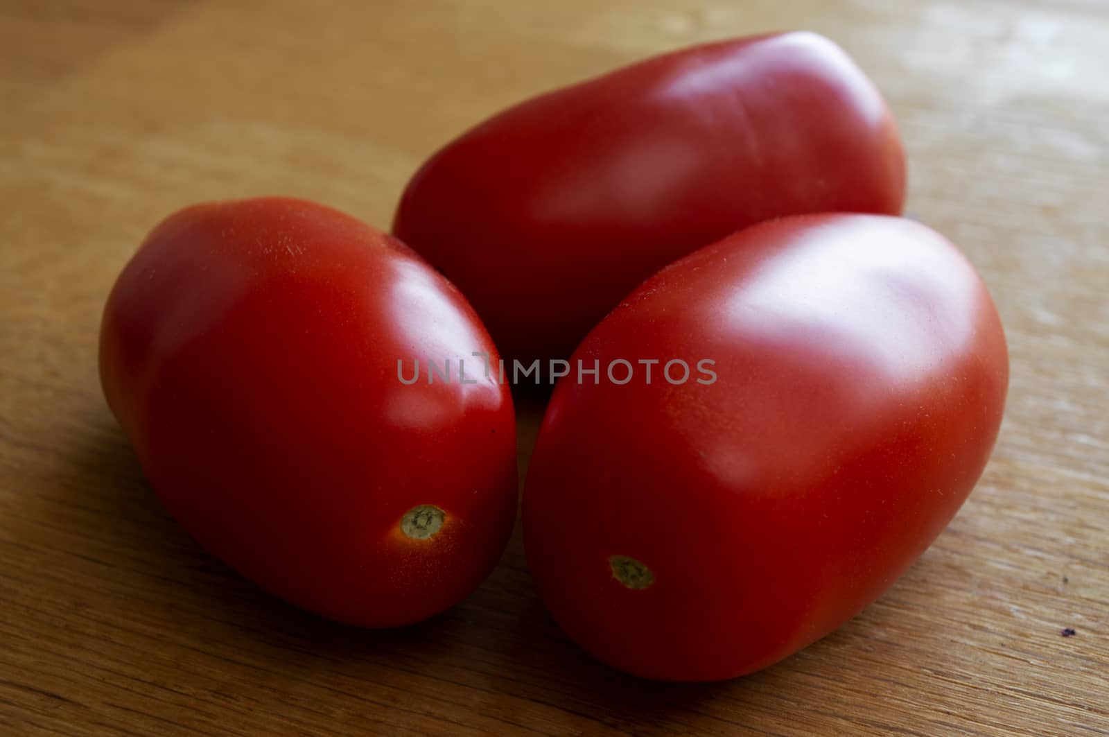 Three red tomatoes on wood table in sunlight.