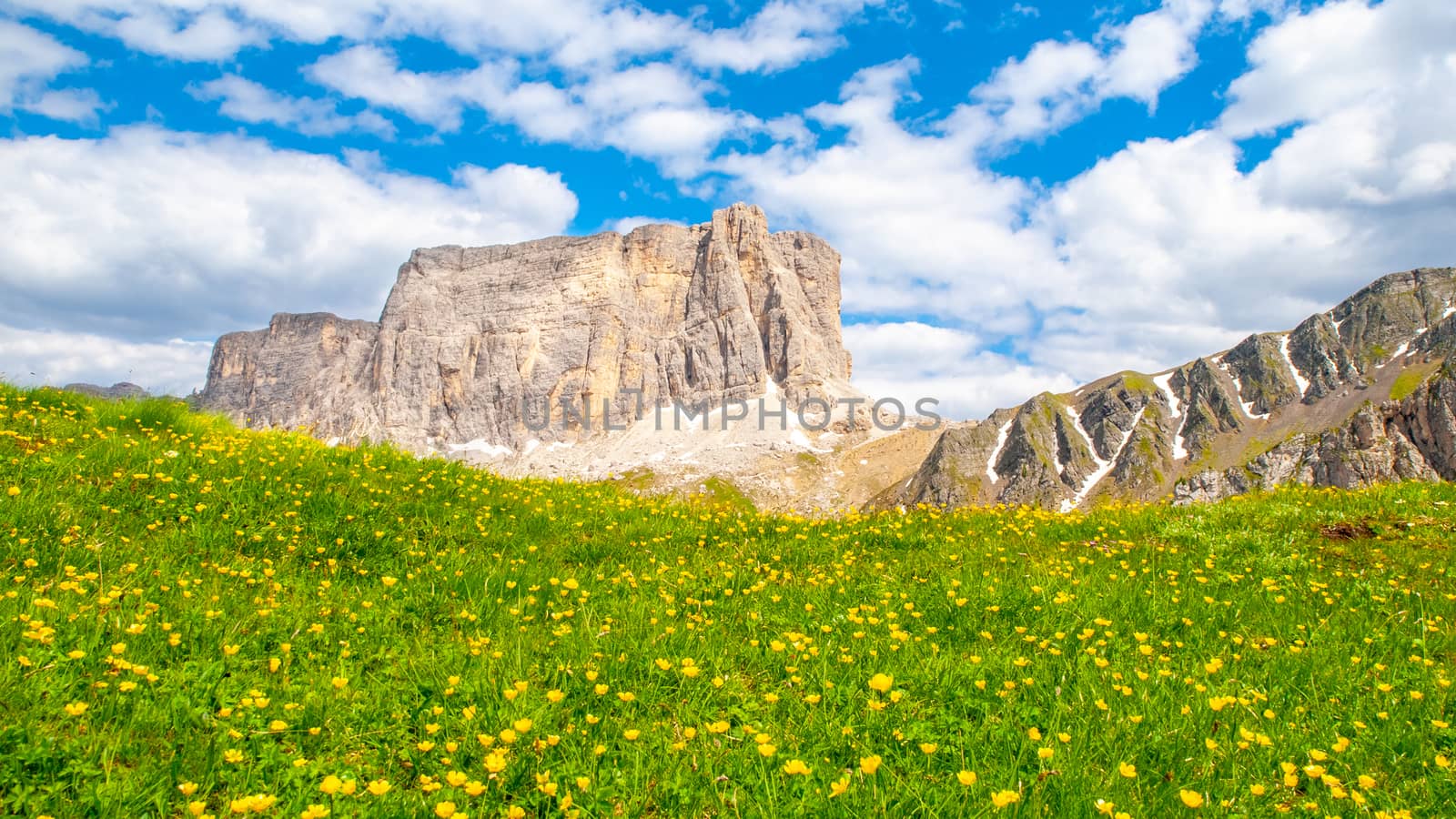 Landscape of Dolomites with green meadows, blue sky, white clouds and rocky mountains.