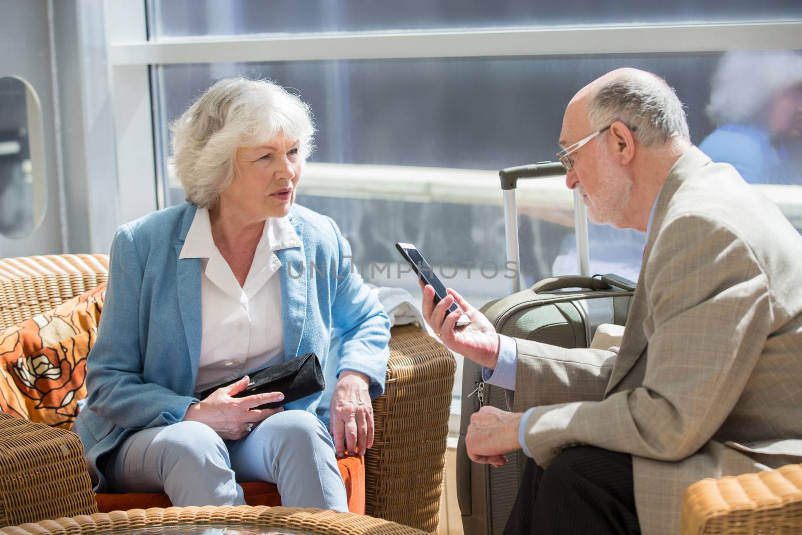 Senior couple of tourists waiting for their flight sitting with suitcase and talking