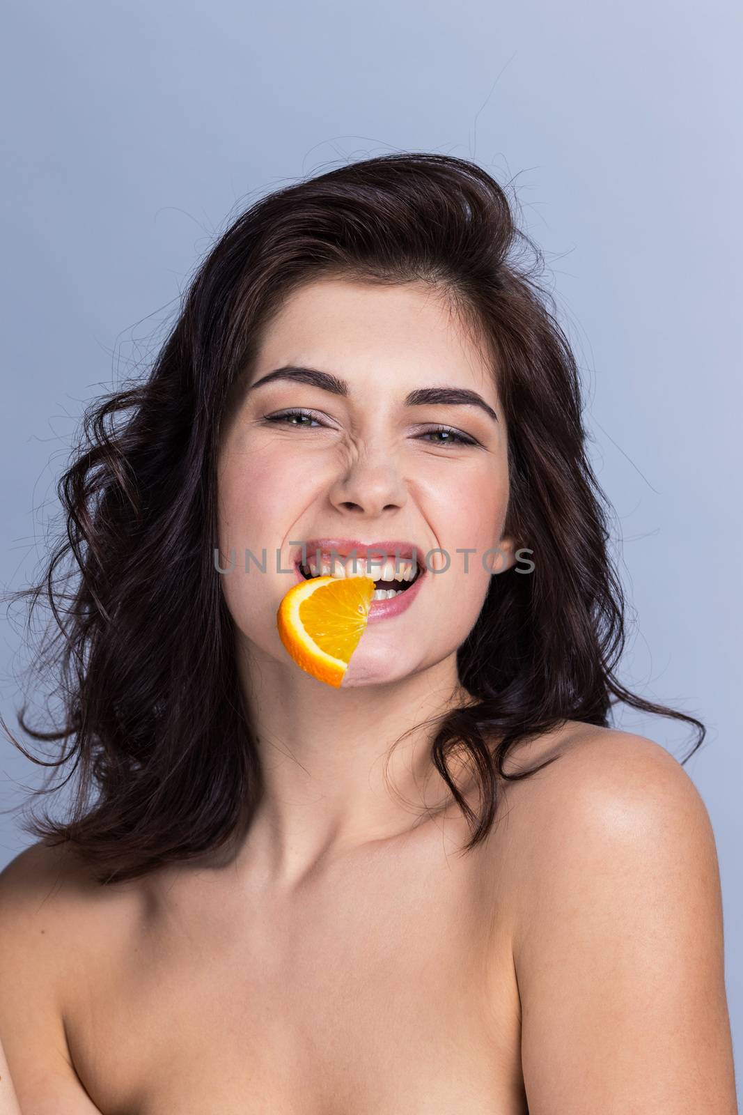 Young funny woman biting slice of orange, healthy eating concept