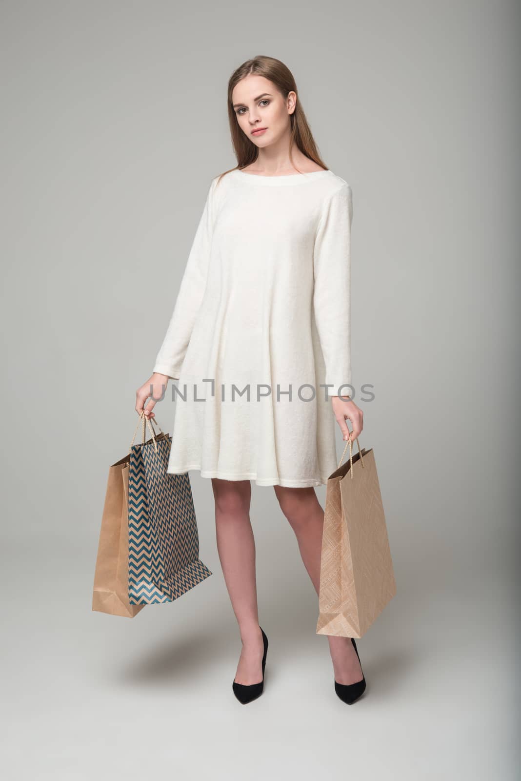 Young model long-haired blond girl in white short dress stands holding shopping packages
