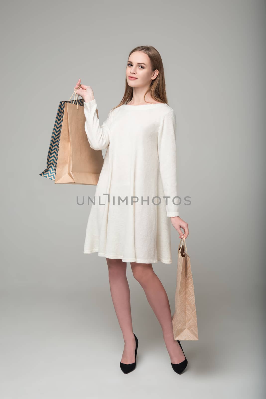 Young model long-haired blond girl in white short dress stands holding shopping packages