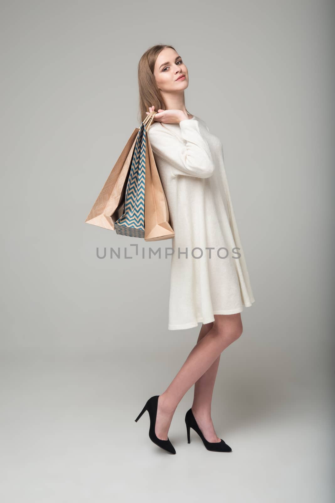 Smiling blond girl in white short dress with paper bags by VeraVerano
