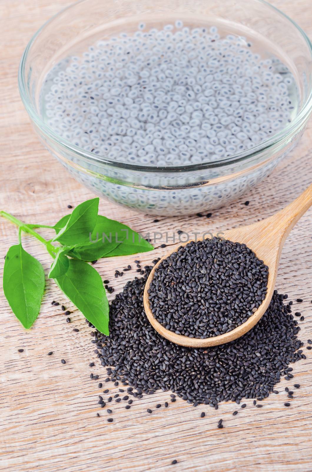 Lemon basil seeds in wooden spoon and soak in water with green leaf on wooden background.