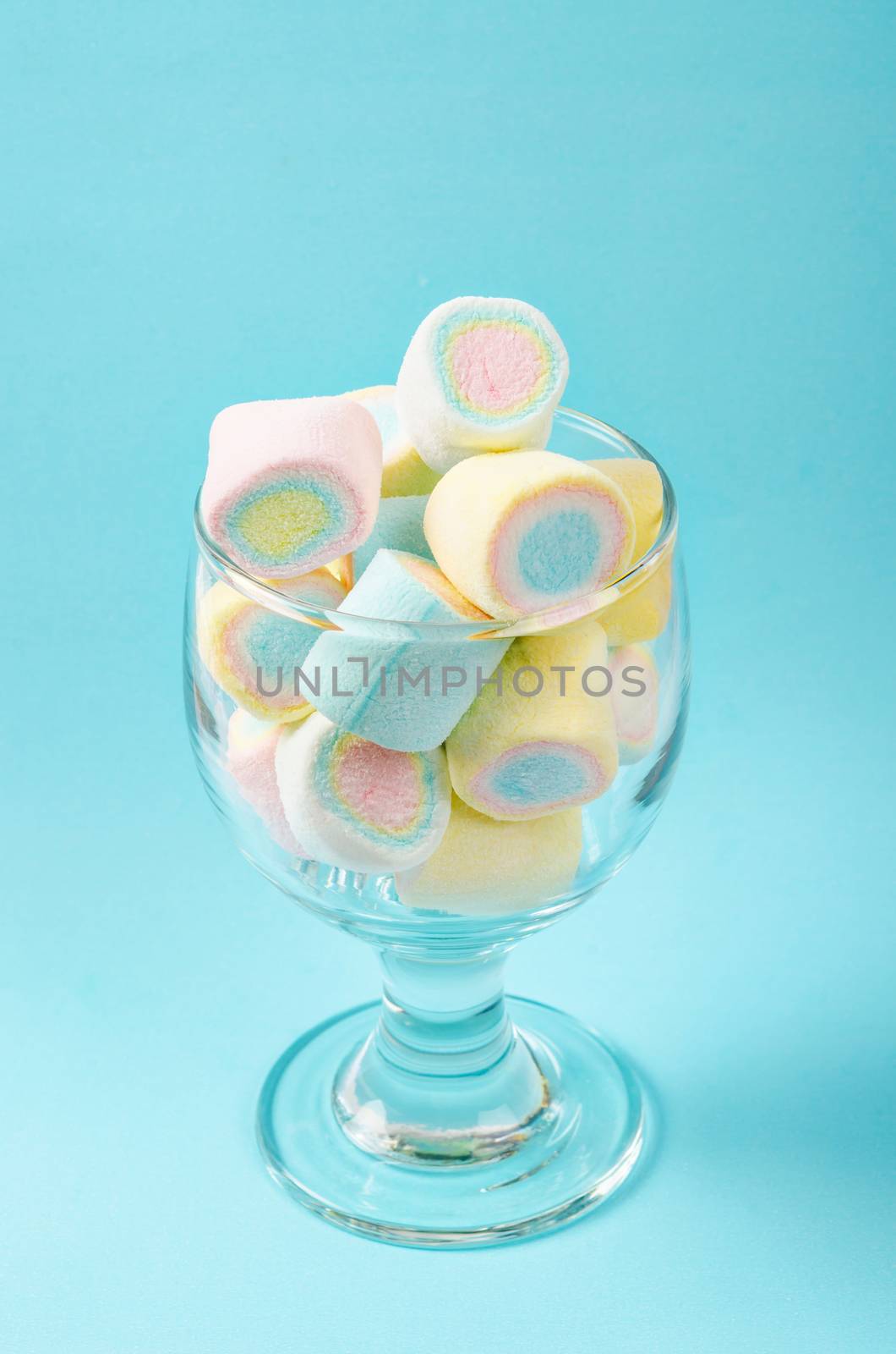 Colorful mini marshmallows in modern glass on blue background.