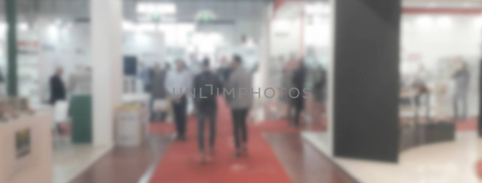 Defocused background of a trade show with people visiting the commercial exhibition. Intentionally blurred post production for bokeh effect