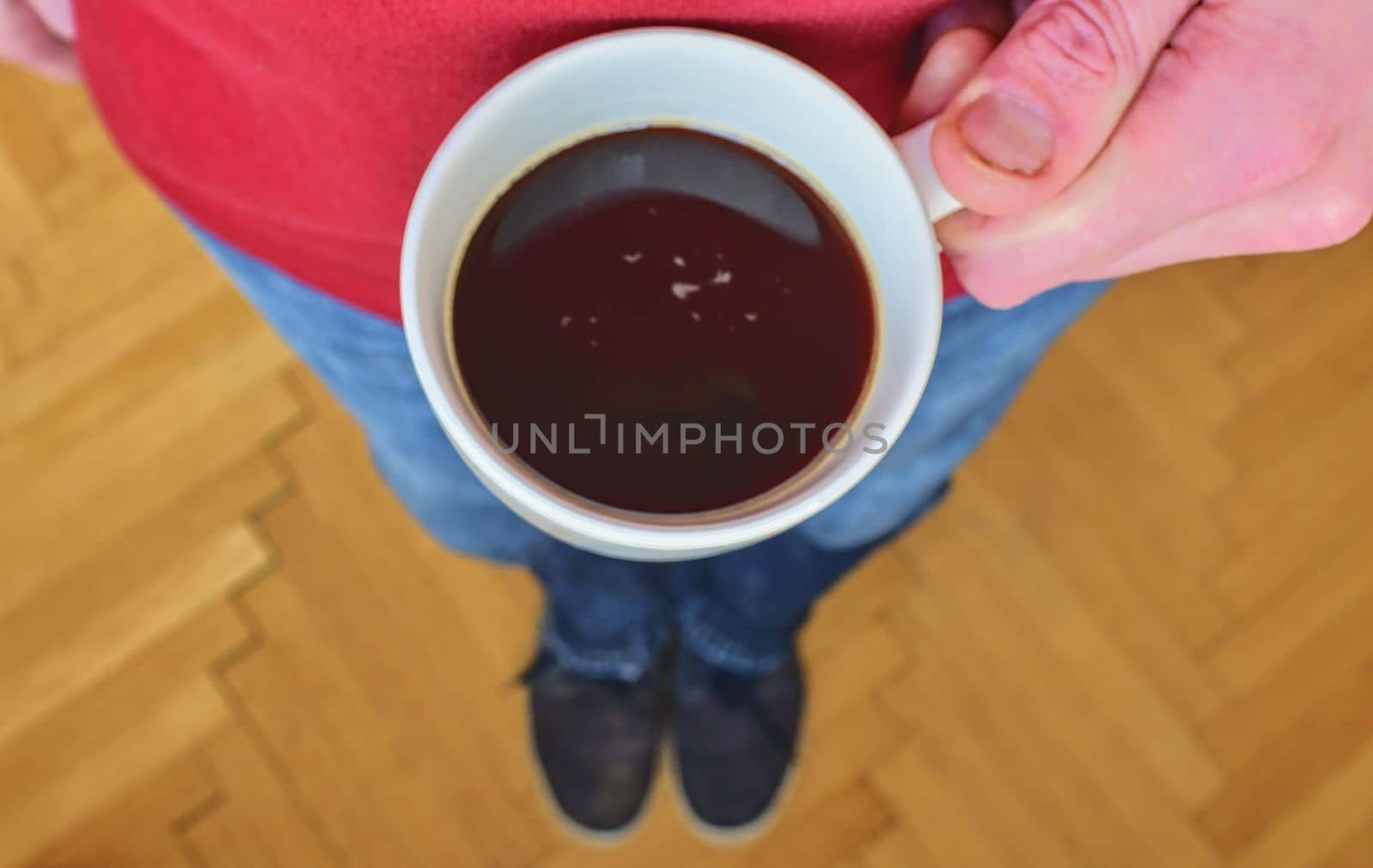 Close up of man hand holding cup of coffee. Man is holding morning cup of coffee. Man with cup of coffee standing on  parquet floor. Close-up. Copy space. Retro colors. 