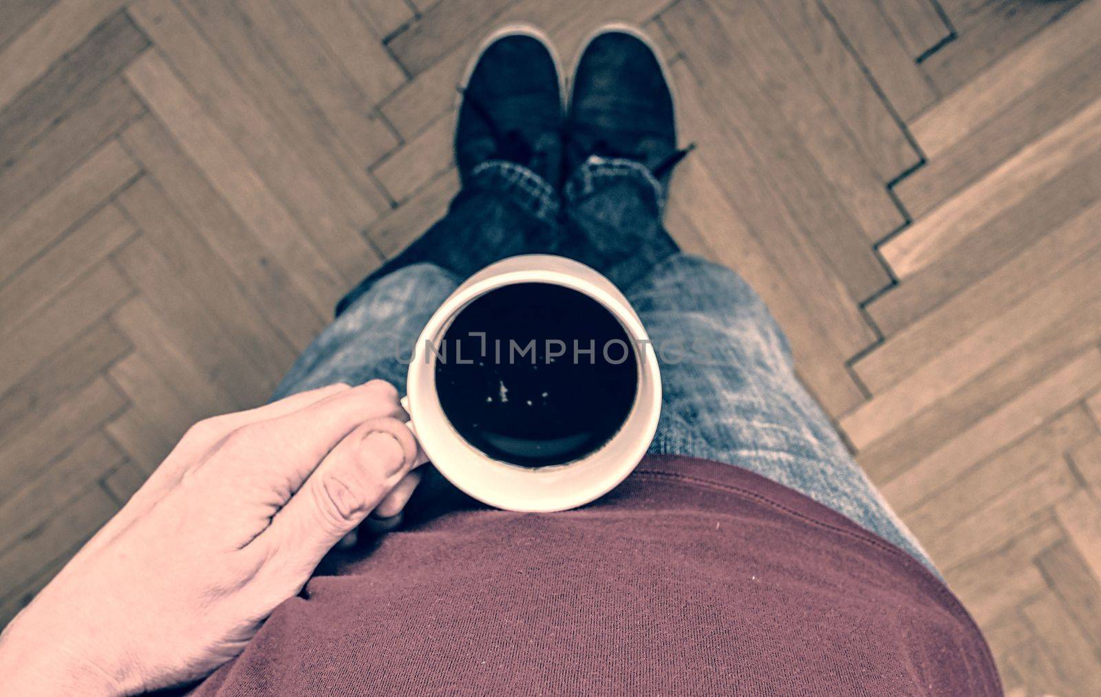 Close up of man hand holding cup of coffee. Man is holding morning cup of coffee. Man with cup of coffee standing on  parquet floor. Close-up. Copy space.