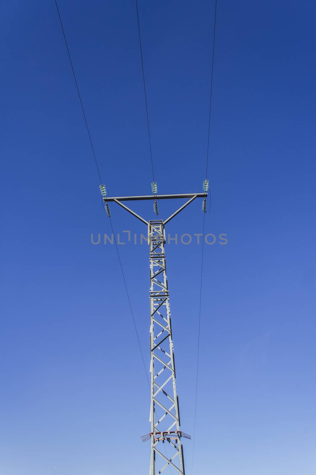 High voltage tower with three cables and blue sky as background