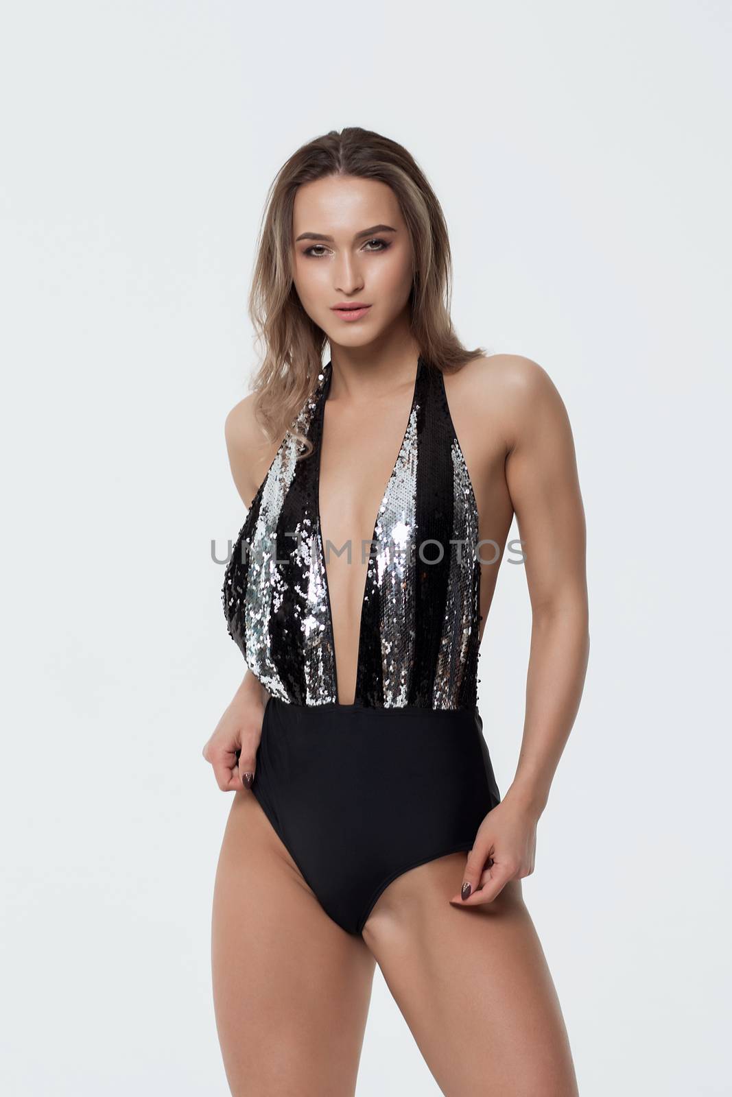 Seductive young woman in beachwear looking at camera and standing on white background in studio
