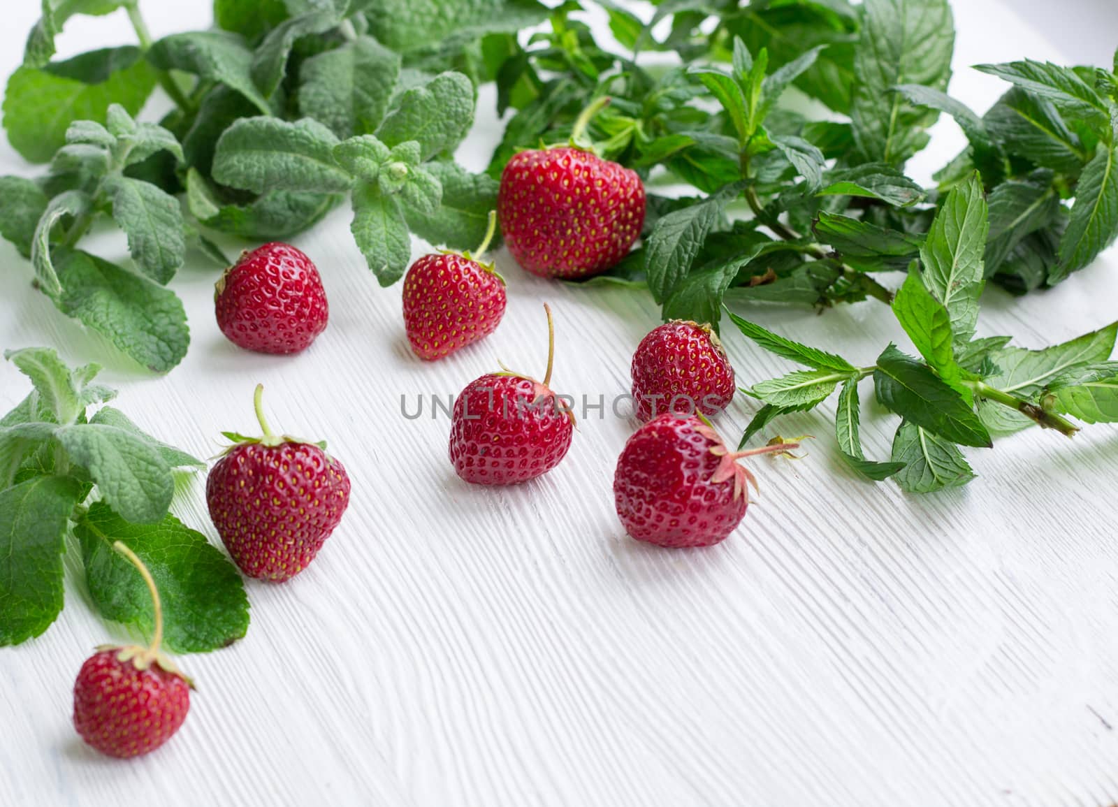 Red strawberries with green herbal mix of fresh mint and melissa herbs on white wooden background