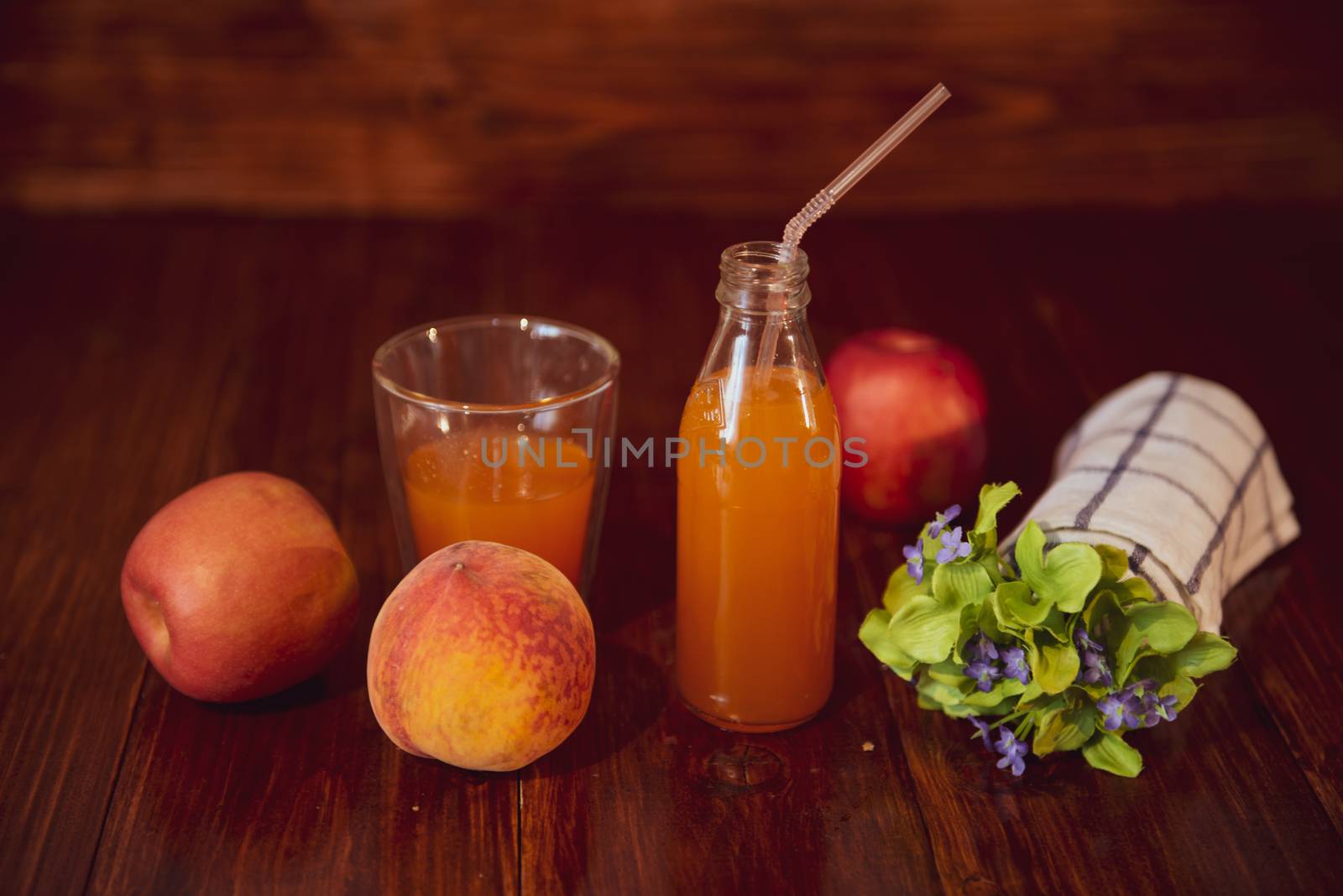 Fresh juice in bottle on wooden table with flowers and fruits