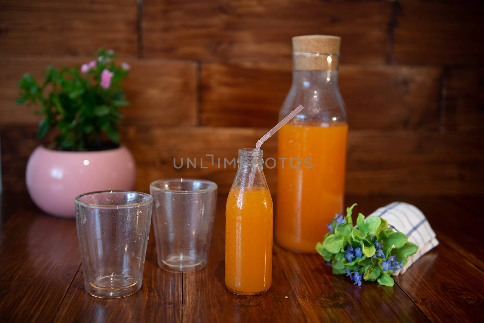 Fresh juice in bottle on wooden table with flowers and two empty glasses