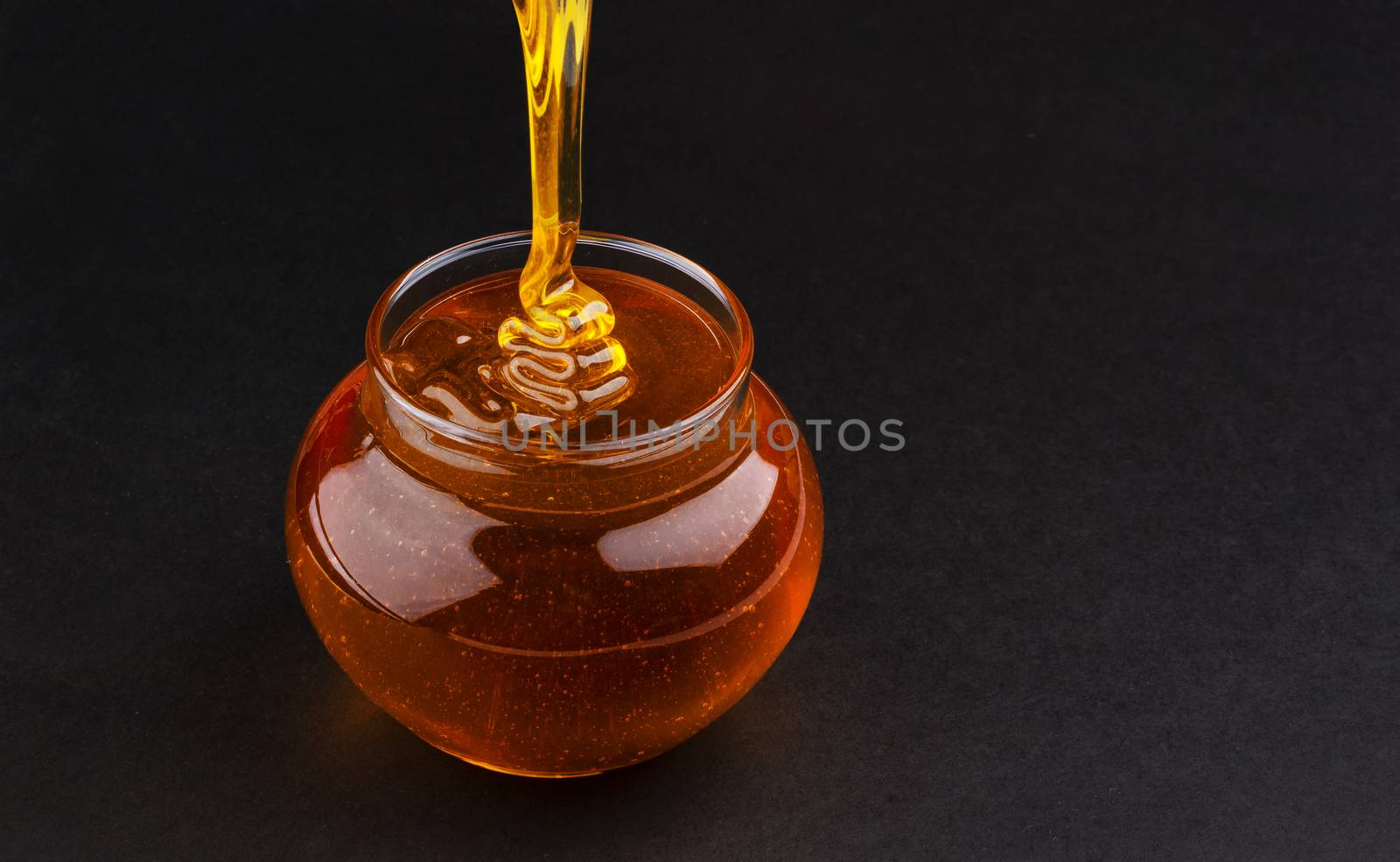Pot of pouring honey on black background with copy space by xamtiw