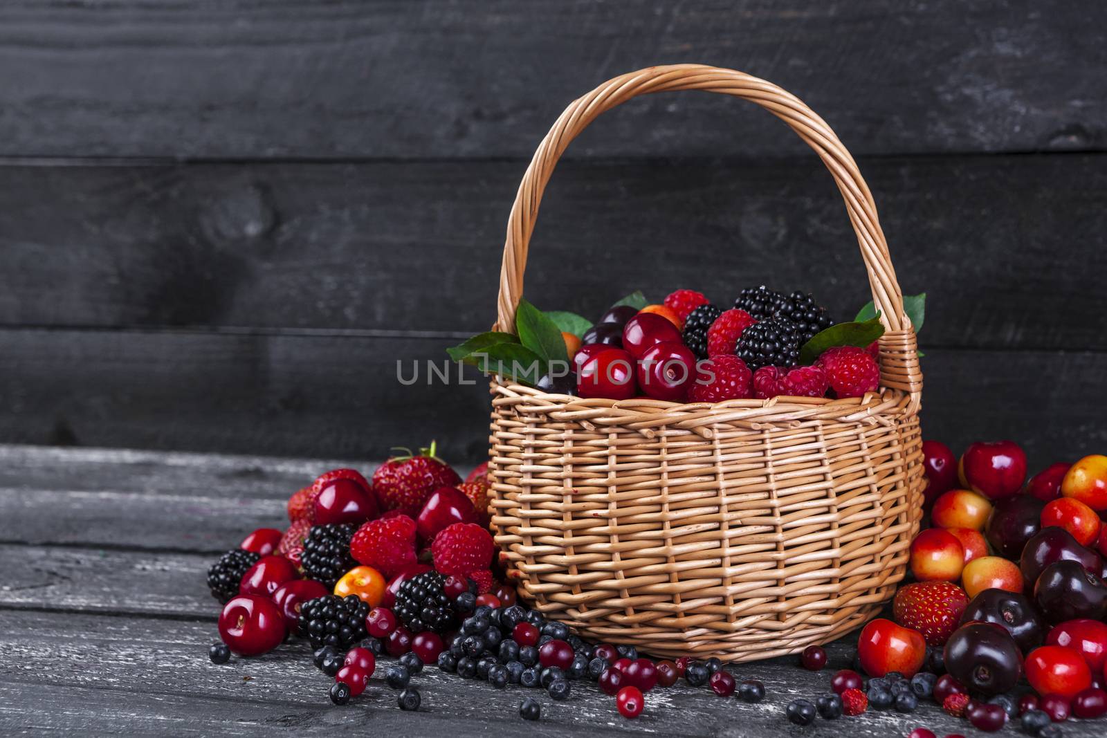 Fresh forest berries in basket on wooden table. Copy space by xamtiw