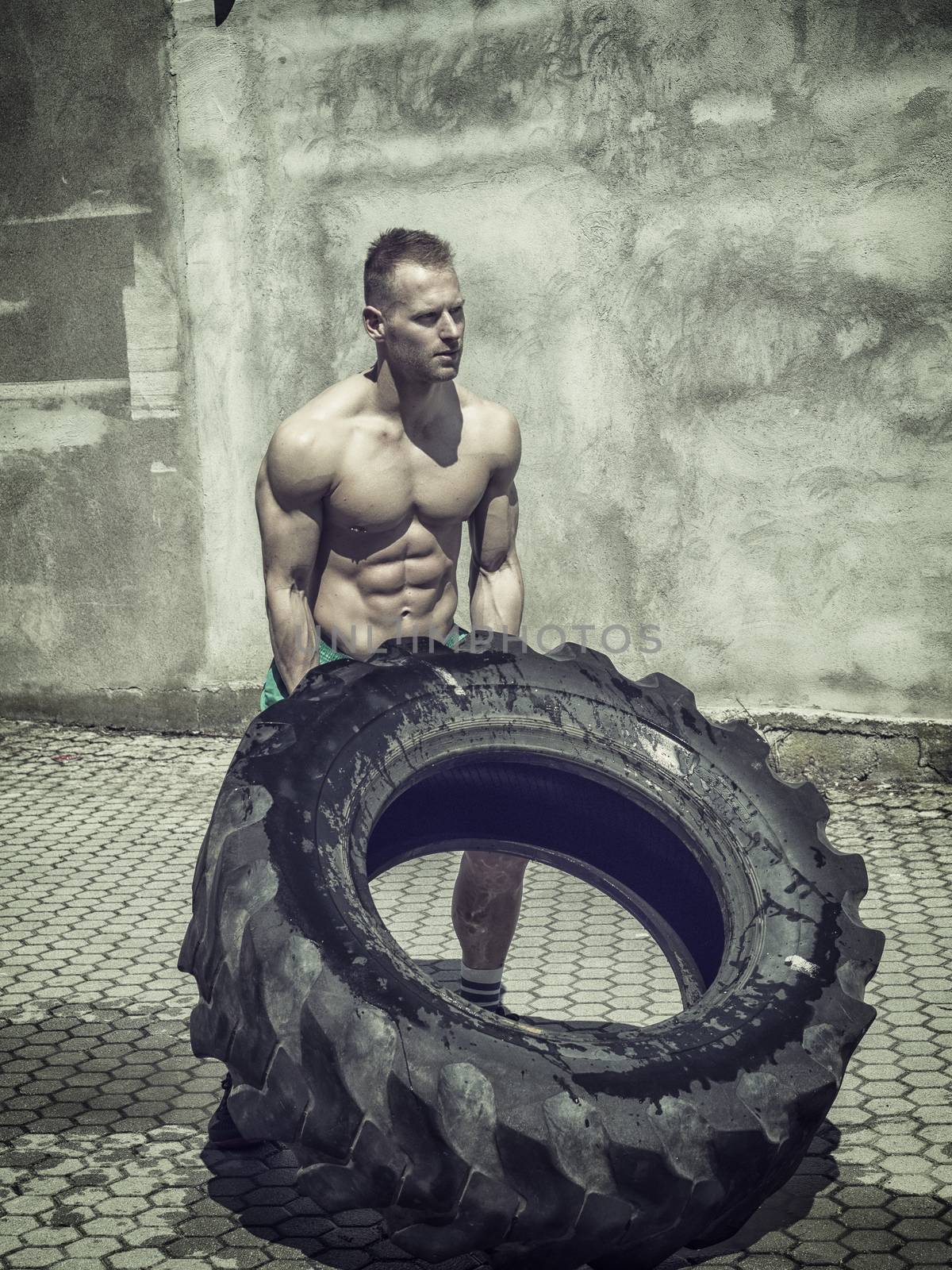 Handsome muscular young man exercising, flipping big tire outdoor