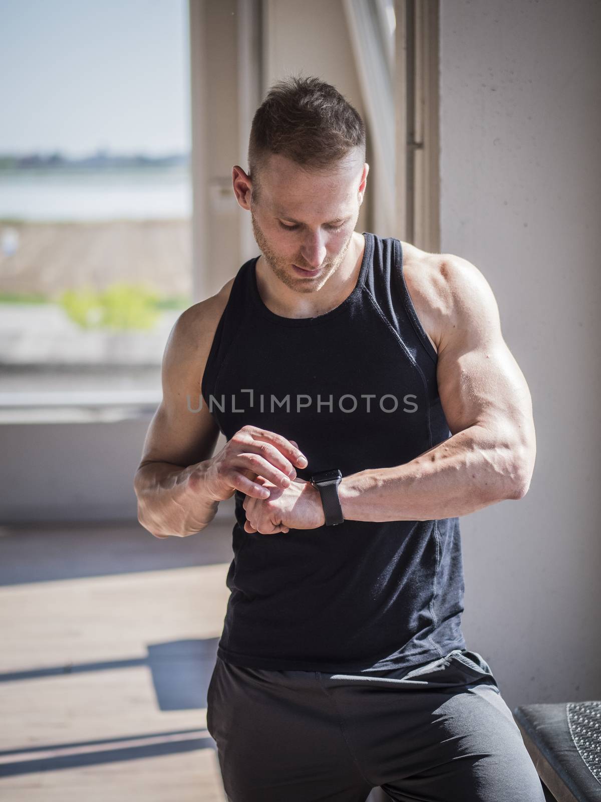 Young attractive man in gym checking sports watch to track his workout, heart pulse or fitness