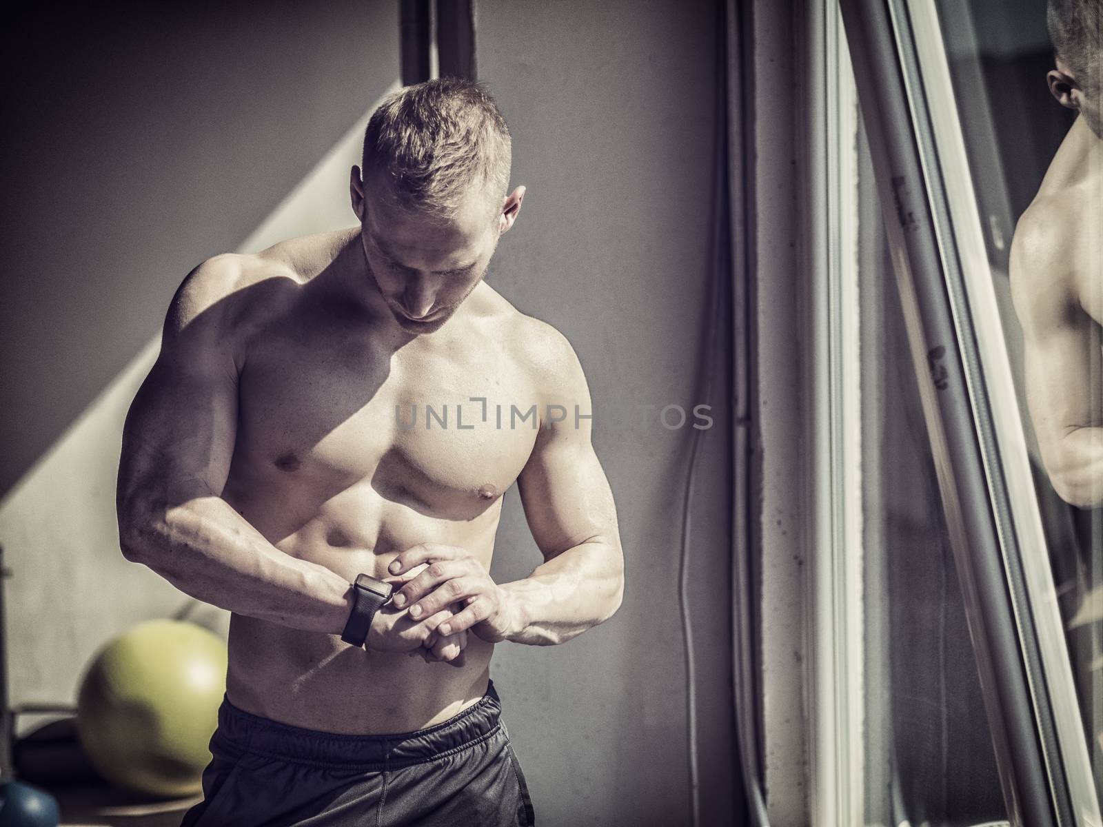 Young attractive man in gym checking sports watch to track his workout, heart pulse or fitness