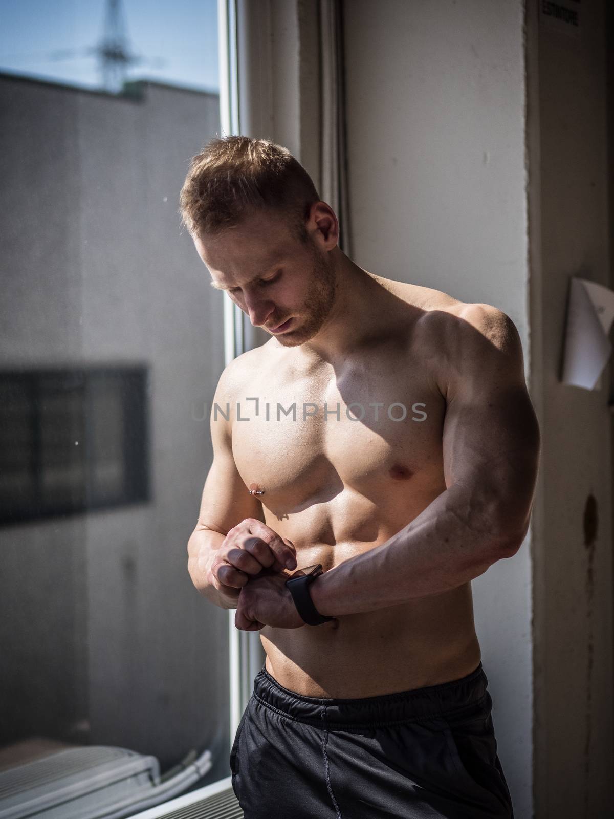 Young attractive man in gym checking sports watch to track his workout, heart pulse or fitness