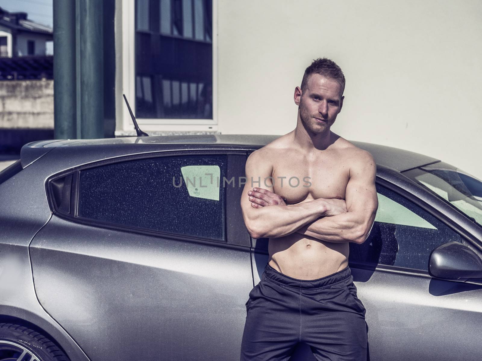 Portrait of young blond handsome muscular topless man leaning on car