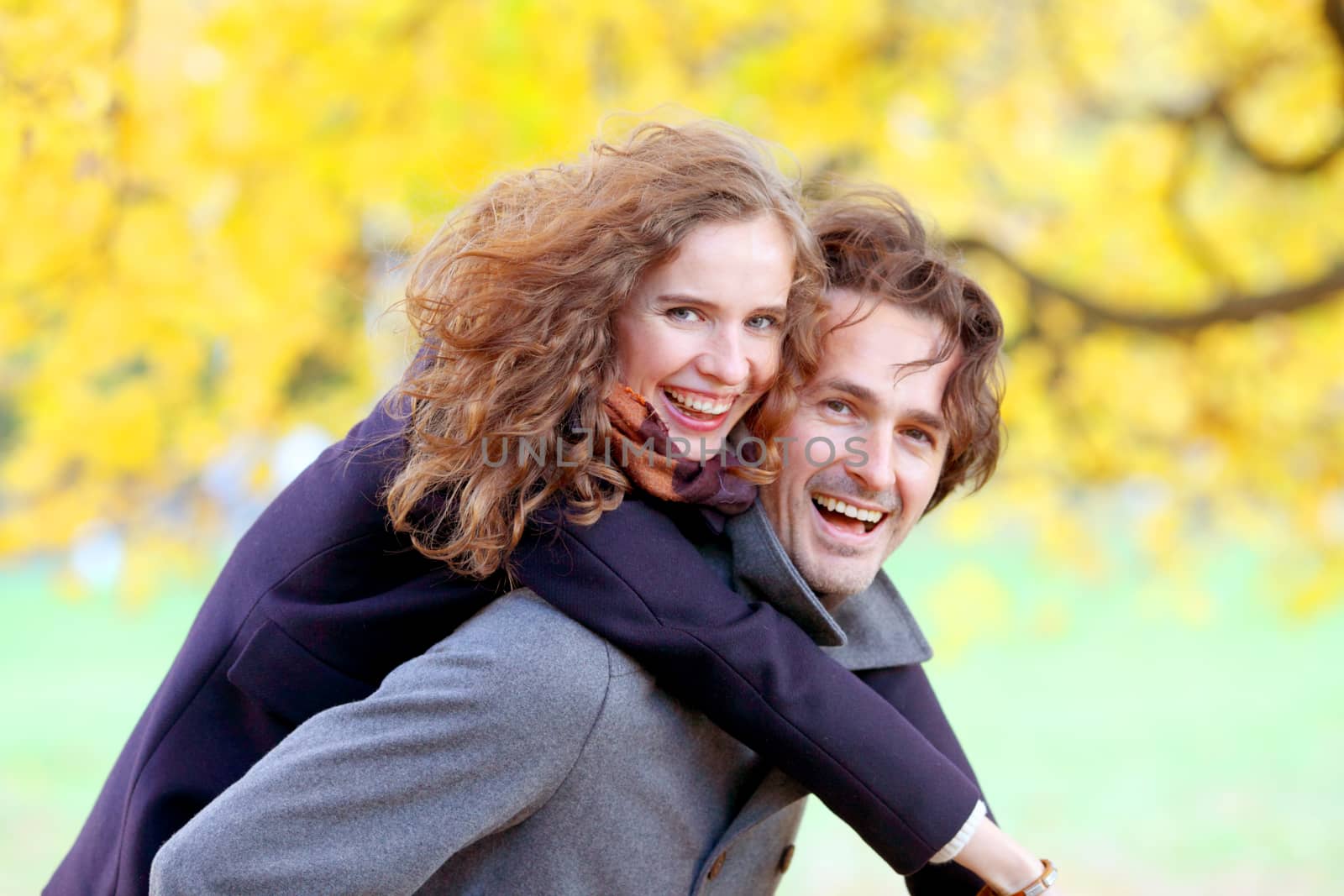 Love, relationships, season and people concept - happy young couple having fun in autumn park piggyback ride