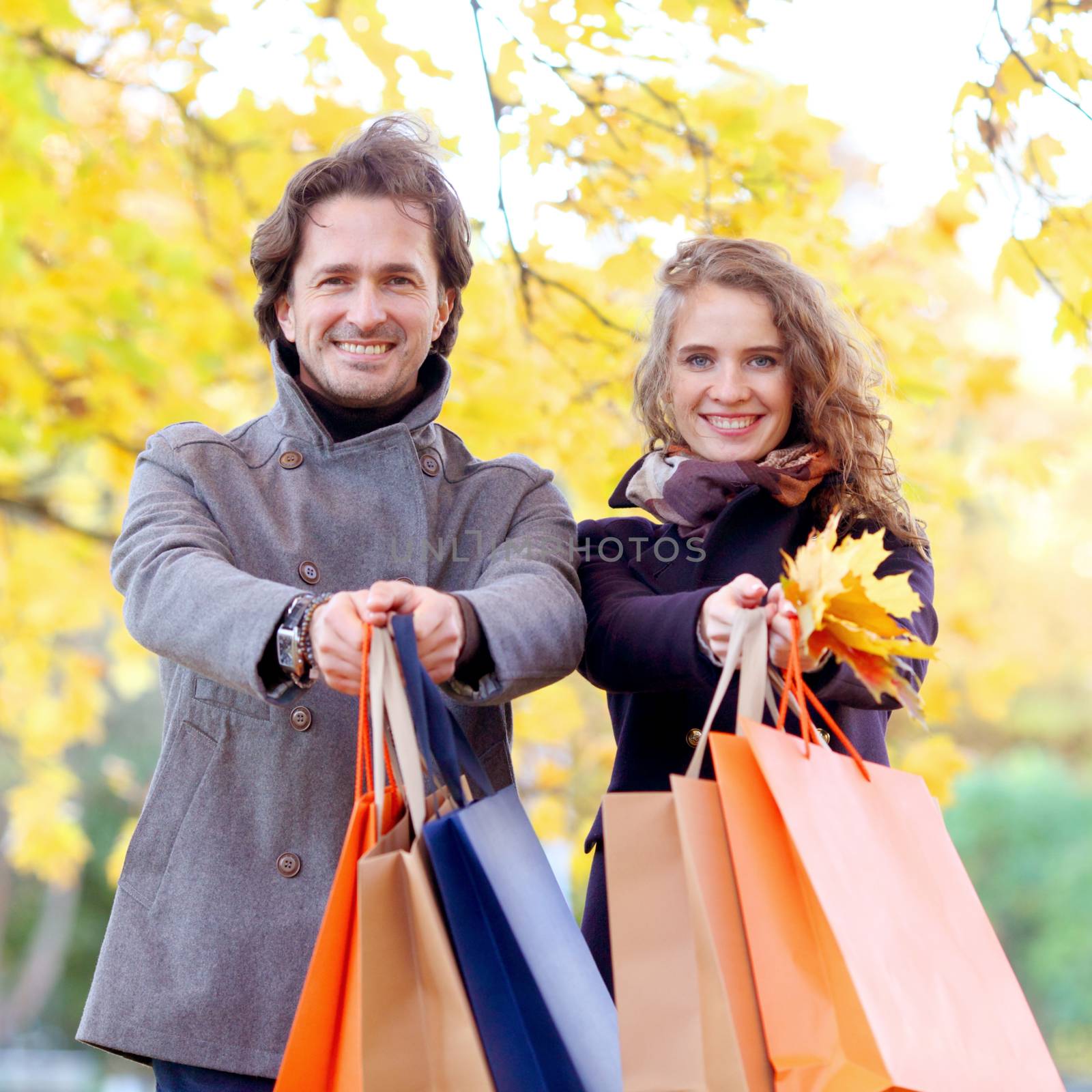 Cheerful couple with shopping bags in autumn park