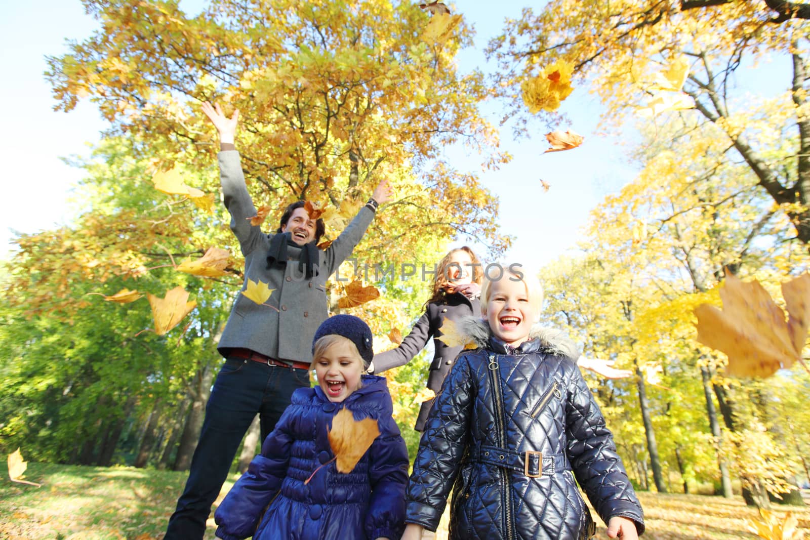 Happy family playing with autumn maple leaves in park