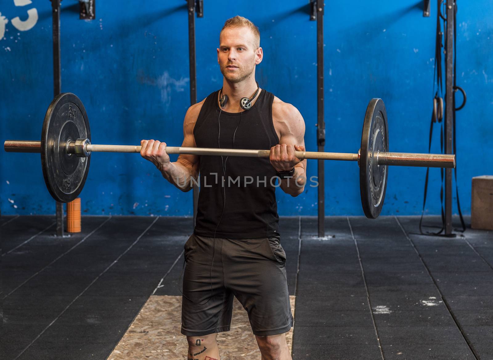 Handsome muscular young man exercising arms in gym with barbell.