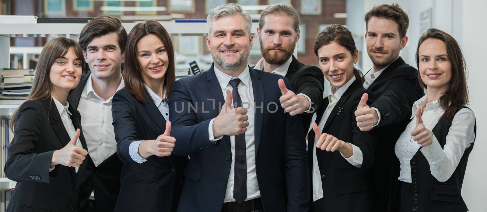 Group of friendly businesspeople with male mature leader in office showing thumbs up sign