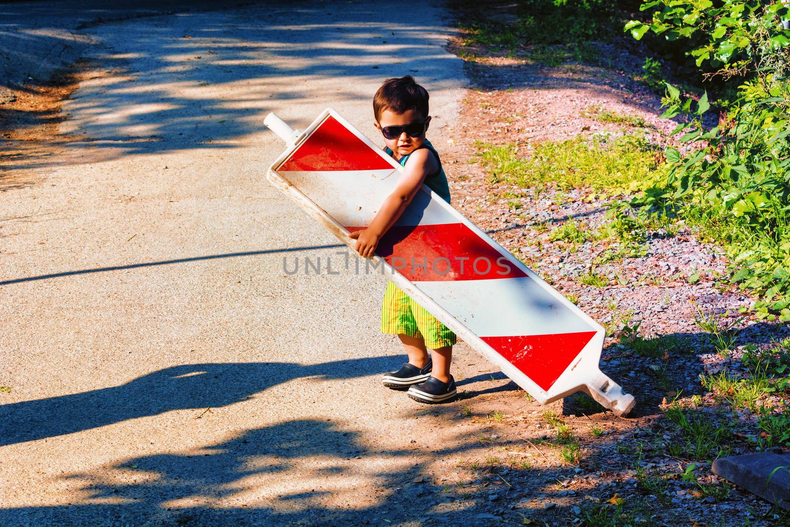 Little boy is carrying a construction site barrier across the street. To overcome difficulties