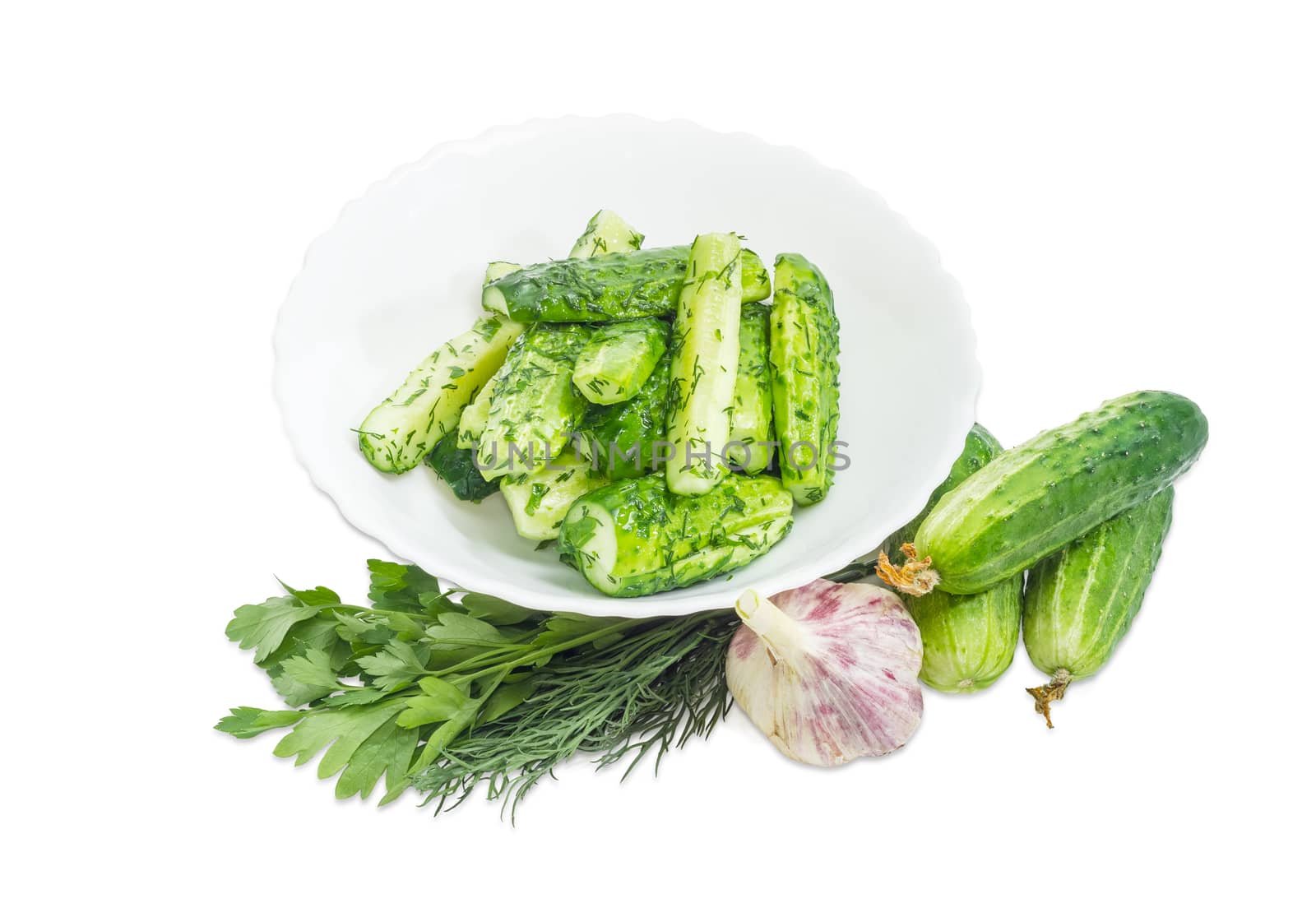 Lightly salted cucumbers on the white dish and several freshly picked out cucumbers, parsley, dill and garlic beside on a white background
