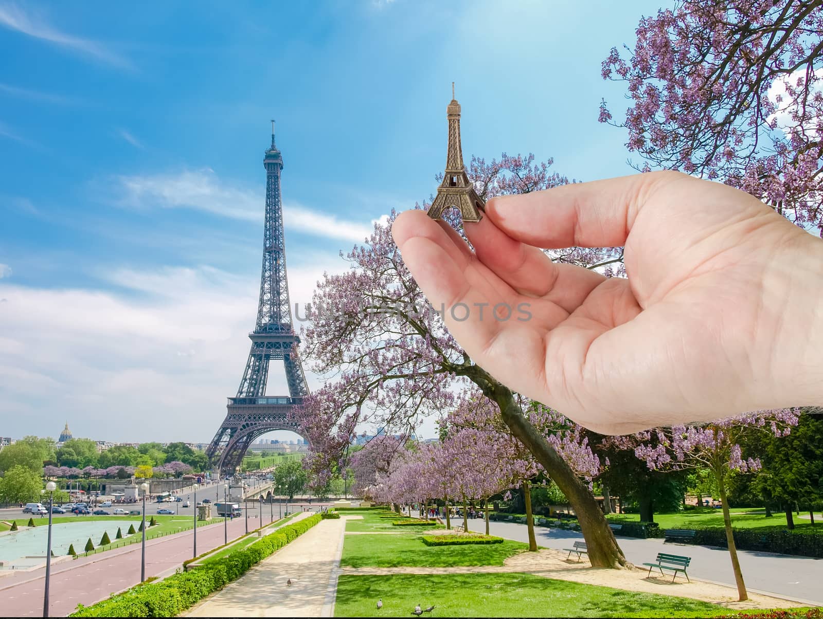 View of the Eiffel Tower from park and  Trocadero Square with small metal Eiffel Tower model in man's hand in a foreground in Paris
