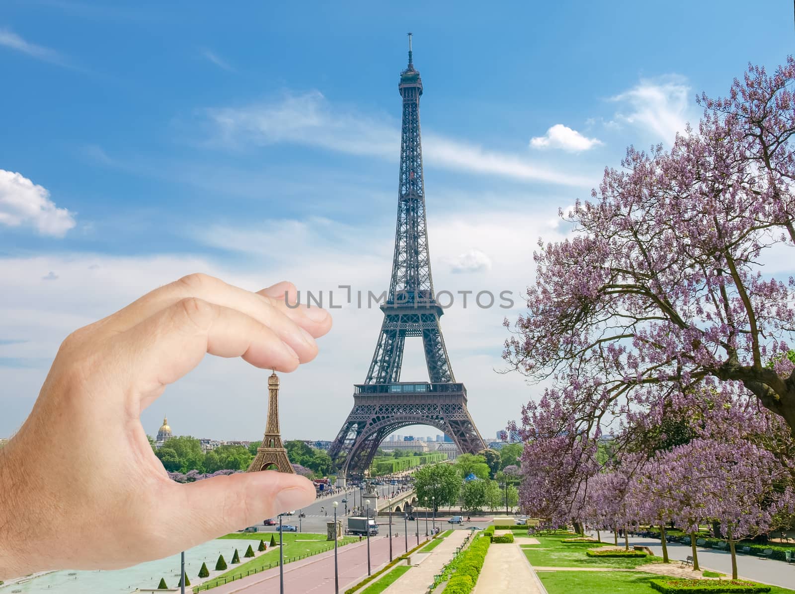 Eiffel Tower with with blossoming trees and small metal Eiffel Tower model in man's hand in a foreground in Paris
