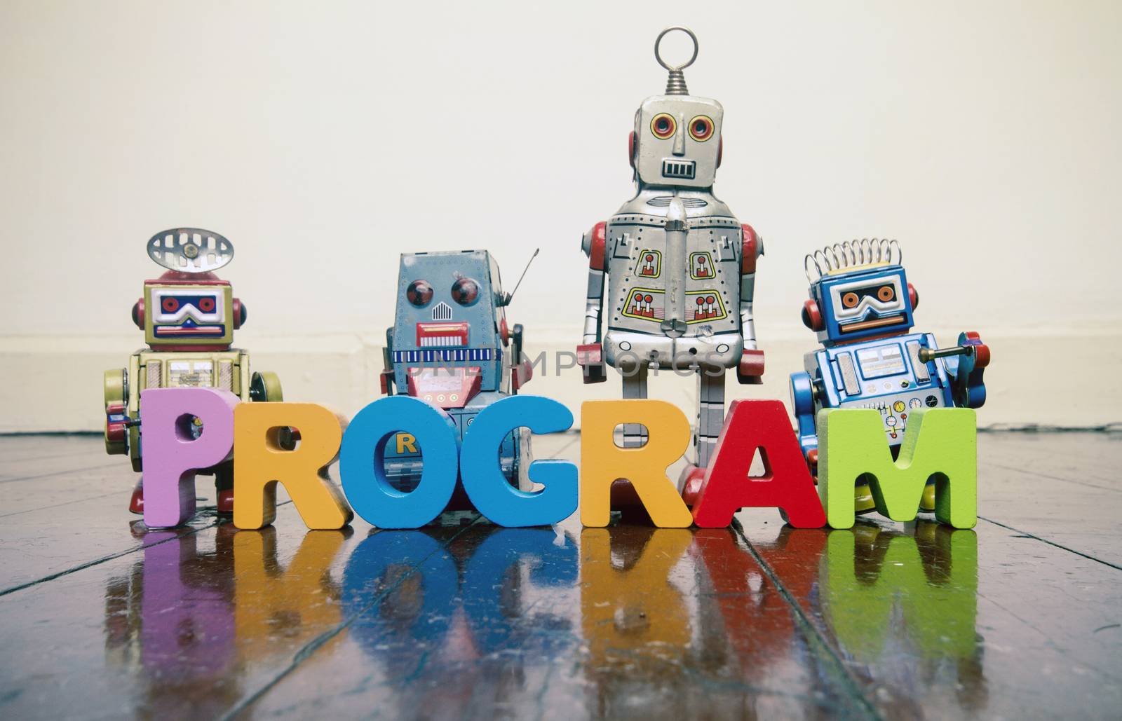 the word PROGRAM with wooden letters and retro toy robots  on an old wooden floor with reflection