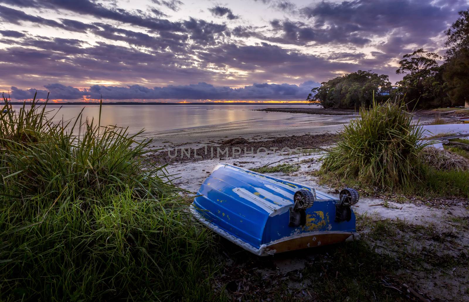 Little blue rowboat, sometimes called "tinnies" in Australia sits upturned on a beach at dawn with the sky aglow with the first colours of morning