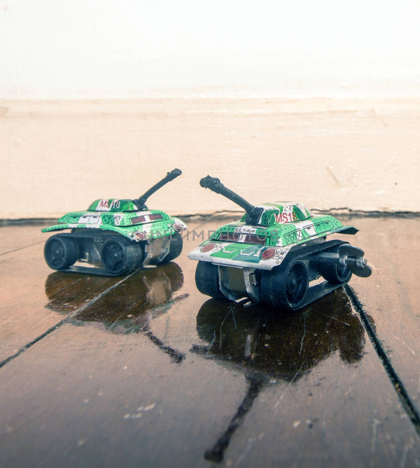 two toy tanks on a wooden floor with reflection