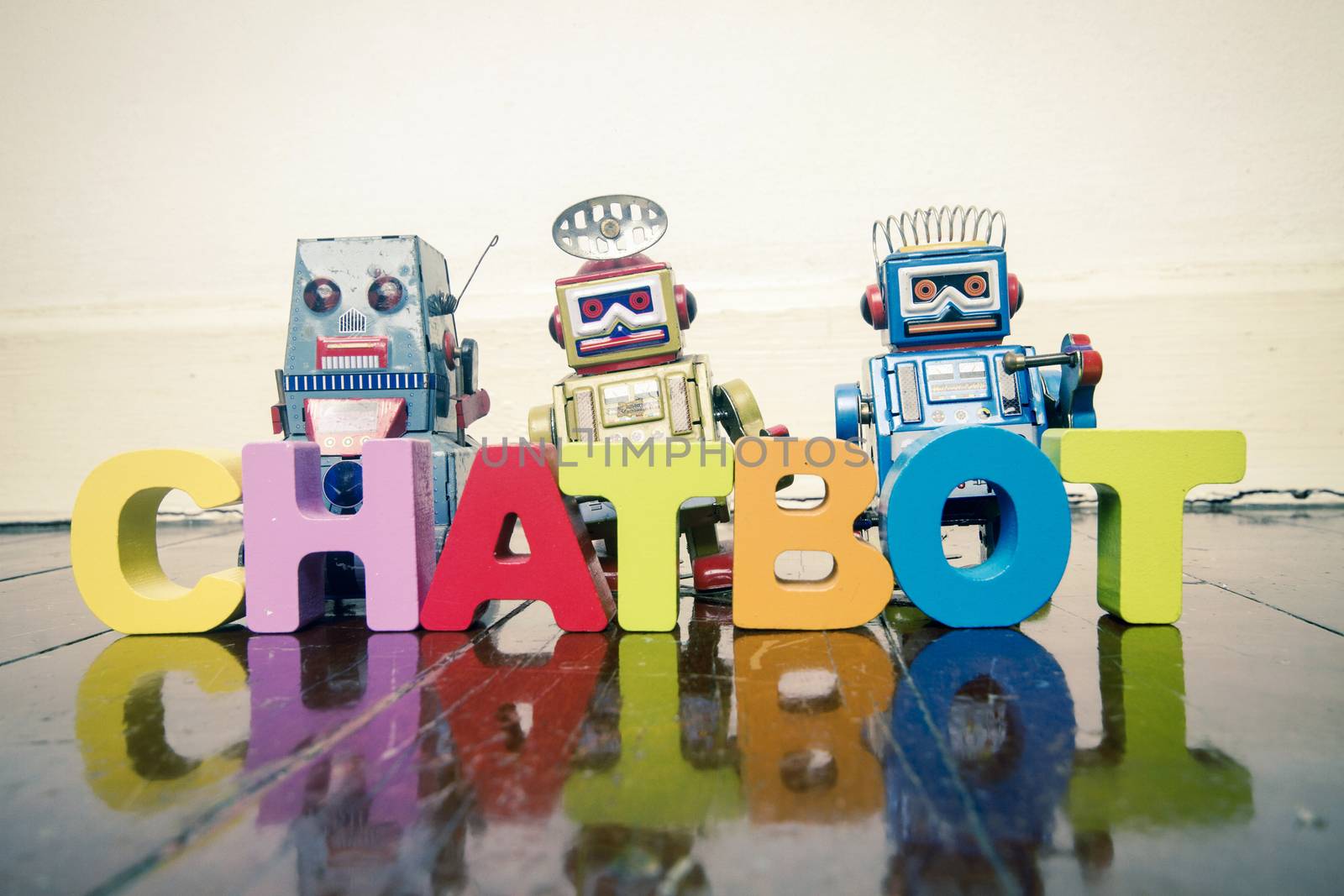 the word  CHAT BOT with wooden letters and retro toy robots  on an old wooden floor with reflection