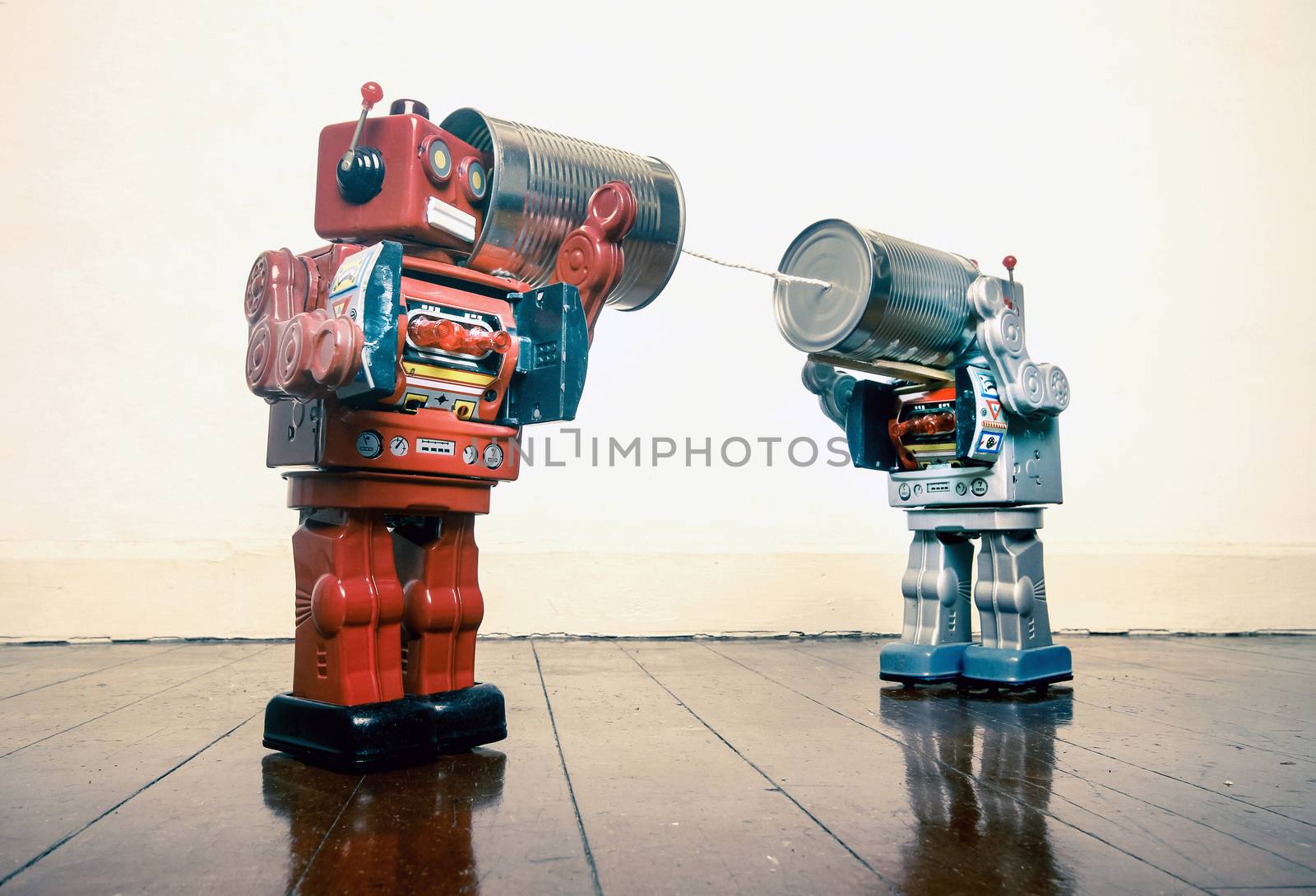 Two retro  Robots toys talking on tin can phones on an old wooden floor 