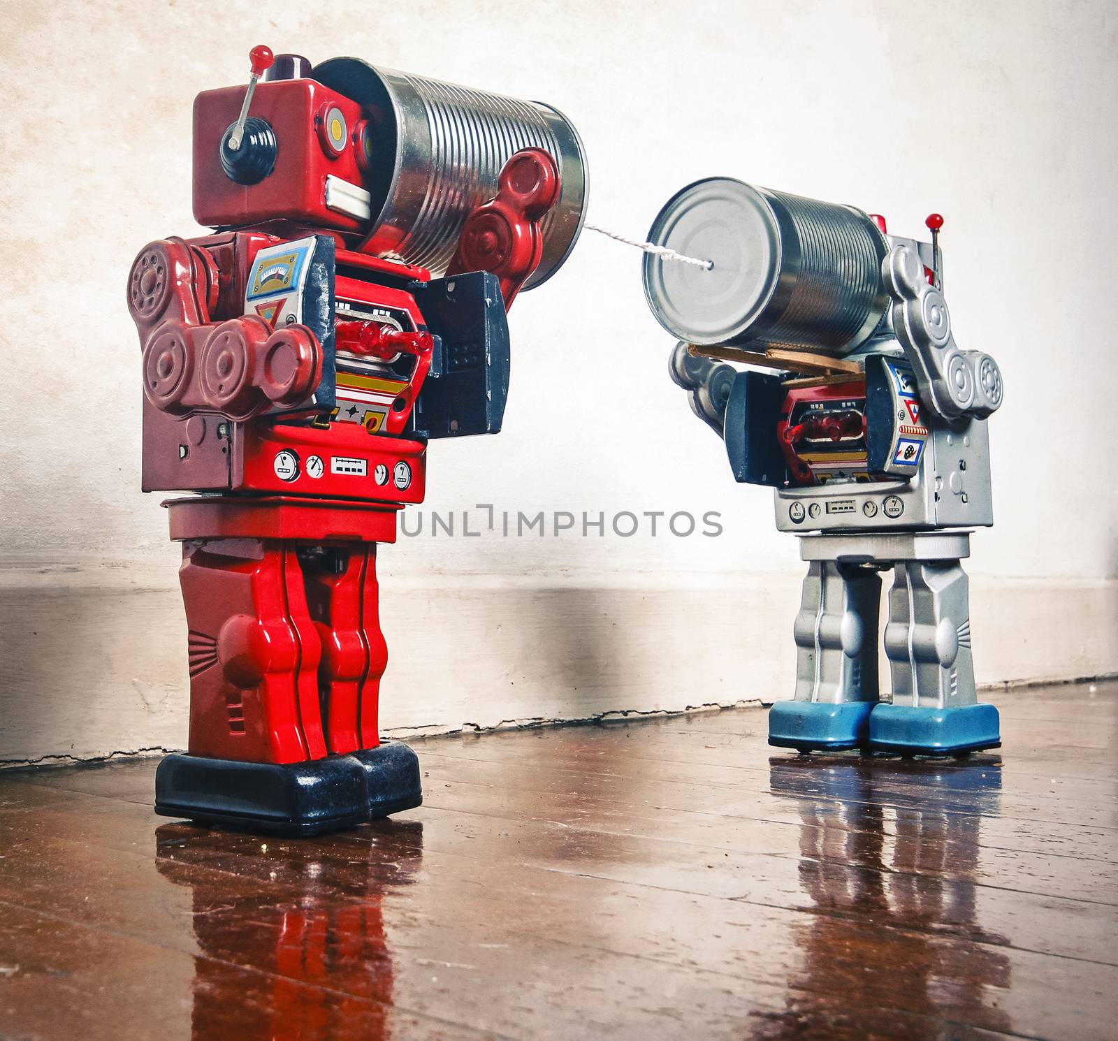 Two retro  Robots toys talking on tin can phones on an old wooden floor 