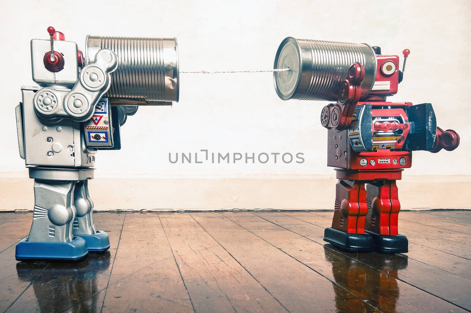 Two retro  Robots toys talking on tin can phones on an old wooden floor 