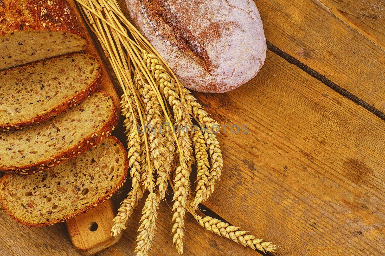 Loafs of bread, slices of bread and ears of grain on wood background. Rustic and rural concept. Close up by roman_nerud