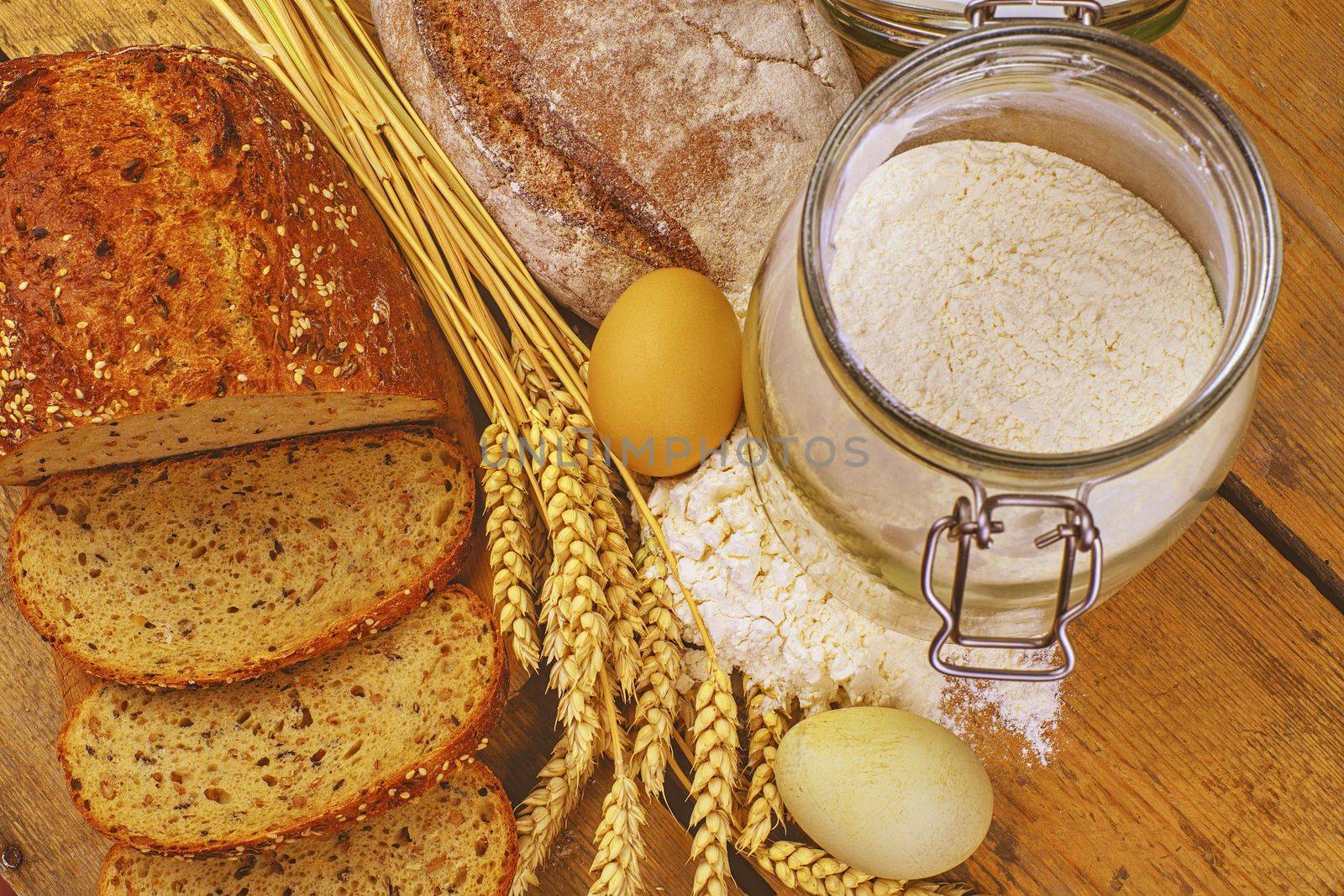 Loafs of bread, slices of bread, wheat flour, eggs and ears of grain on wood background. Rustic and rural concept. Close up. Flat lay.  