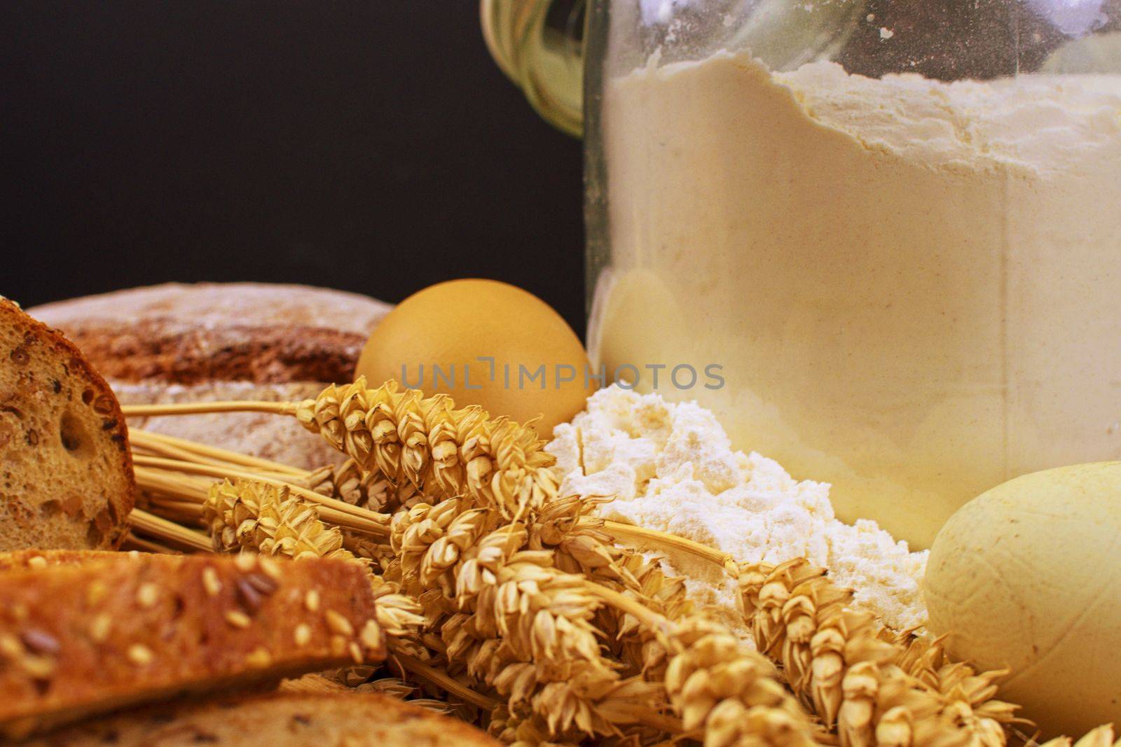 Loafs of bread, slices of bread, wheat flour, eggs and ears of grain on wood background. Rustic and rural concept. Close up. Copy space.