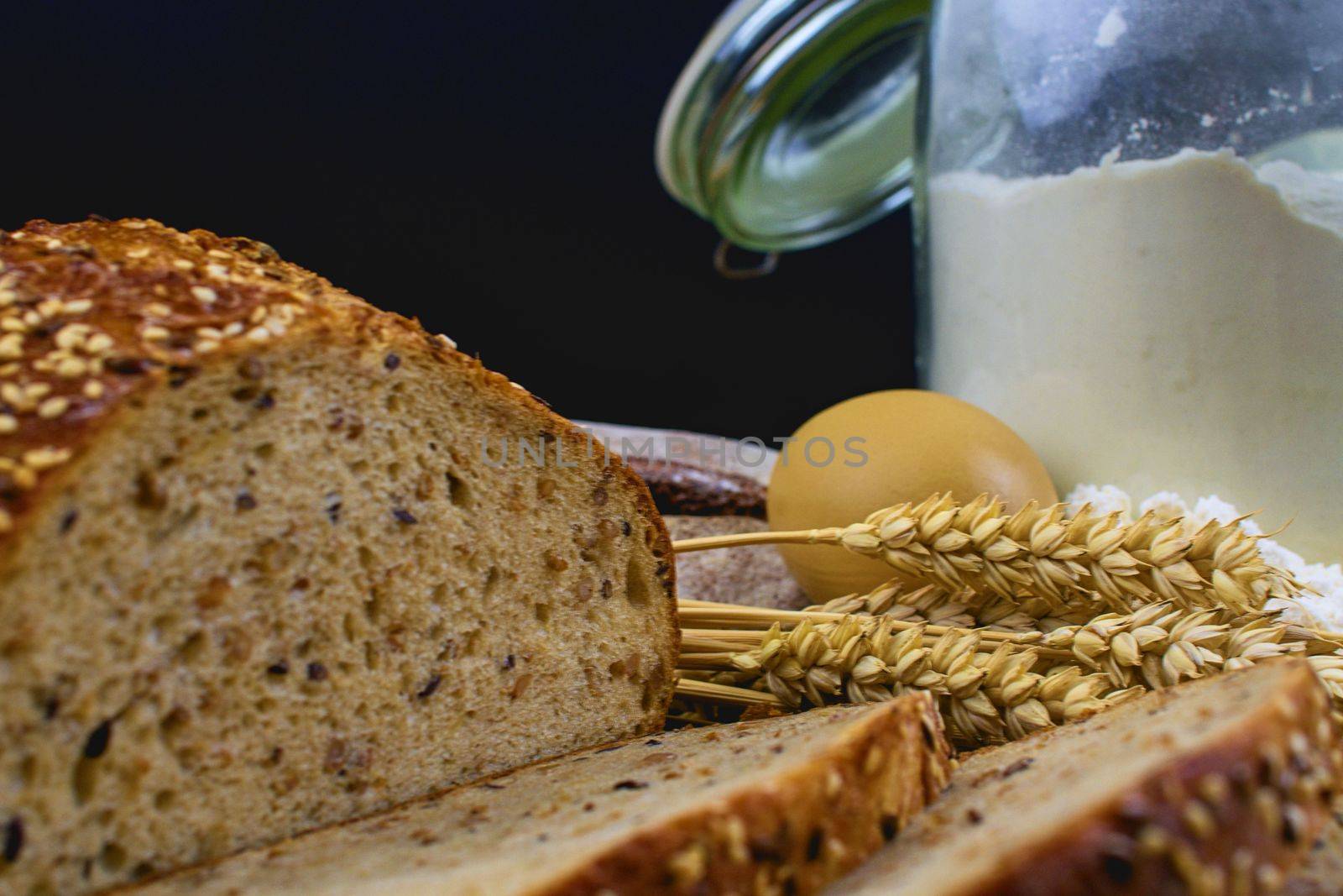 Loafs of bread, slices of bread, wheat flour, eggs and ears of grain on wood background. Rustic and rural concept. Close up. Copy space by roman_nerud