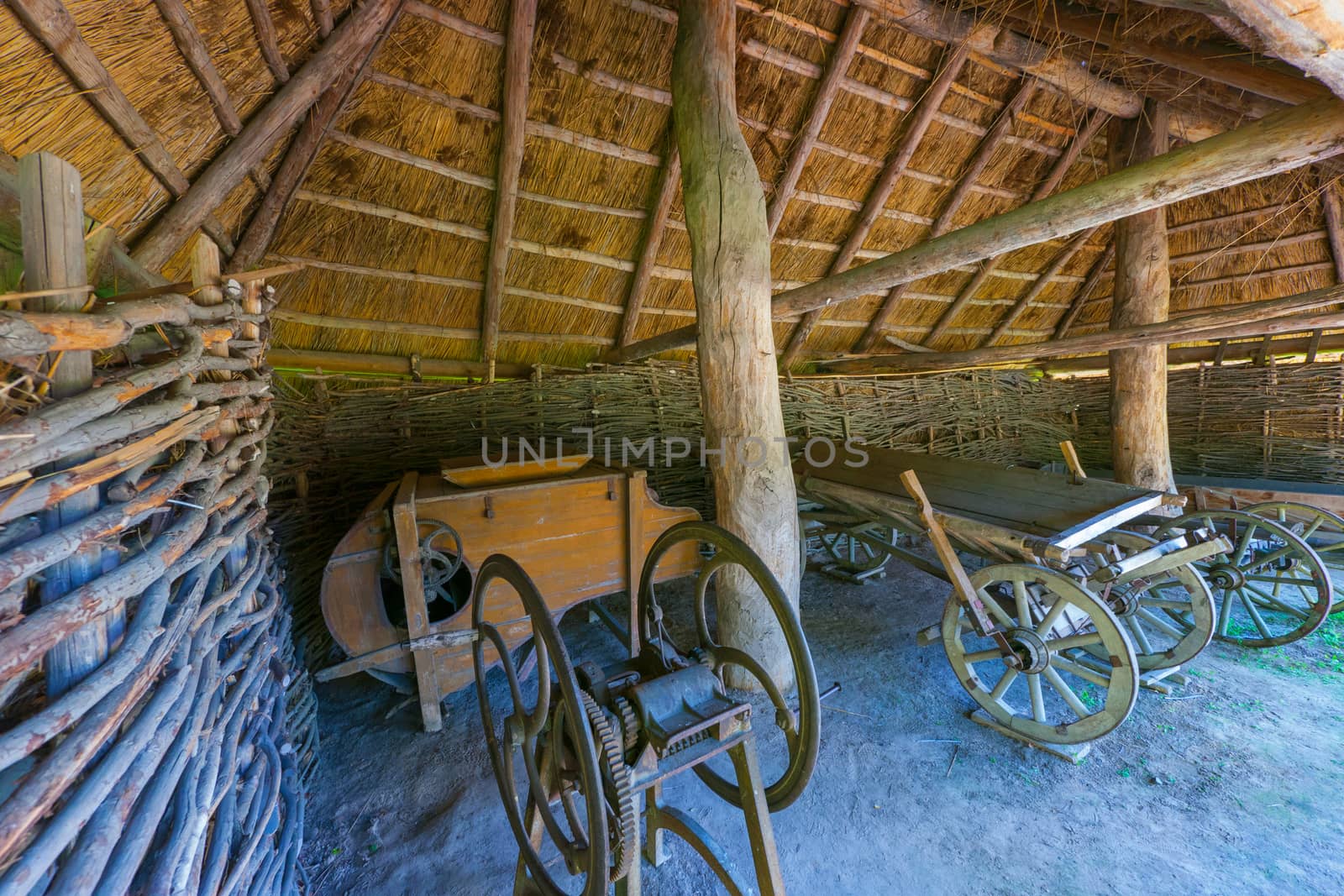 An ancient device for cutting grass, a cart with wooden wheels and an iron hoop on top of them. Standing in a barn with a thatched roof