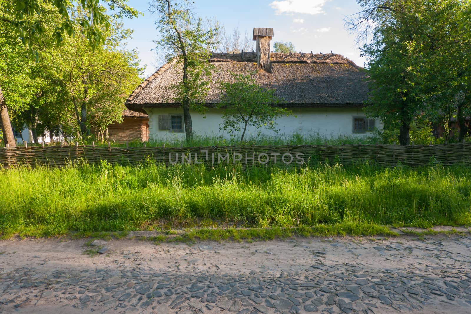 Stone road passing near the old Ukrainian house with a wicker fence and a green garden