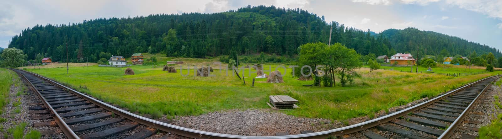 A steep turn of the railway on the glade near the village, which is located near the mountains