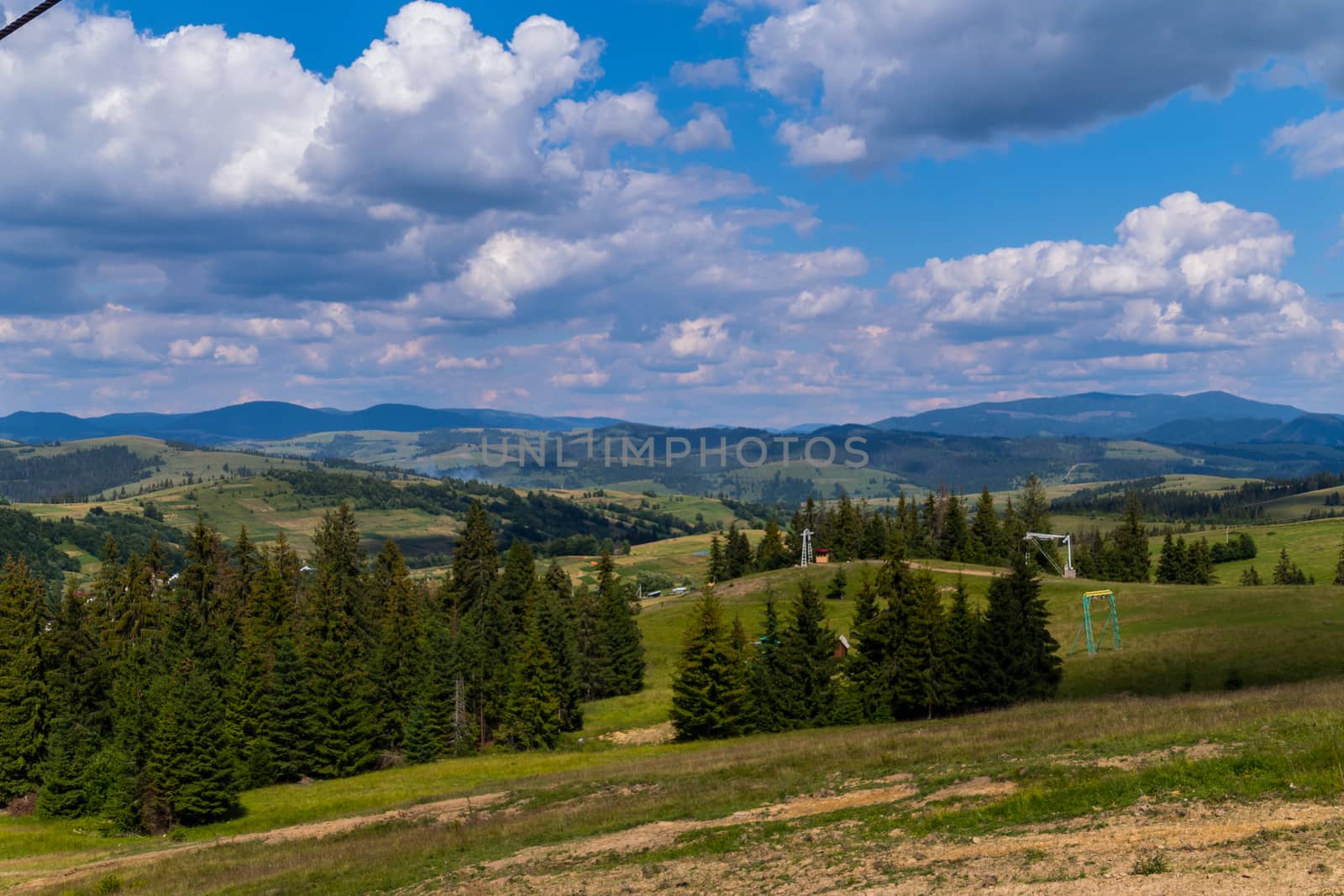 mountain landscape, green slopes, and, ski lifts against a cloudy blue sky